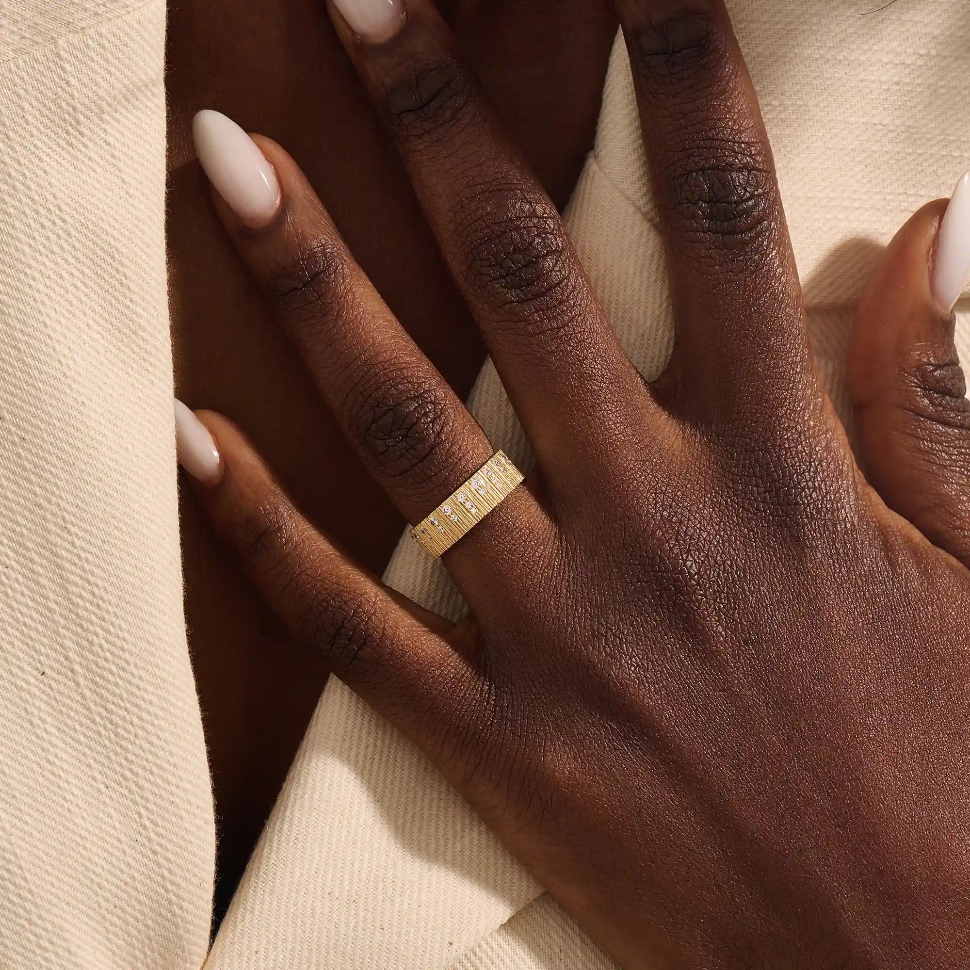 Close-up of a woman wearing a 14k solid yellow gold wide wedding band with wood grain texture and pavé set round brilliant cut moissanite stones, distinctive and modern statement jewelry
