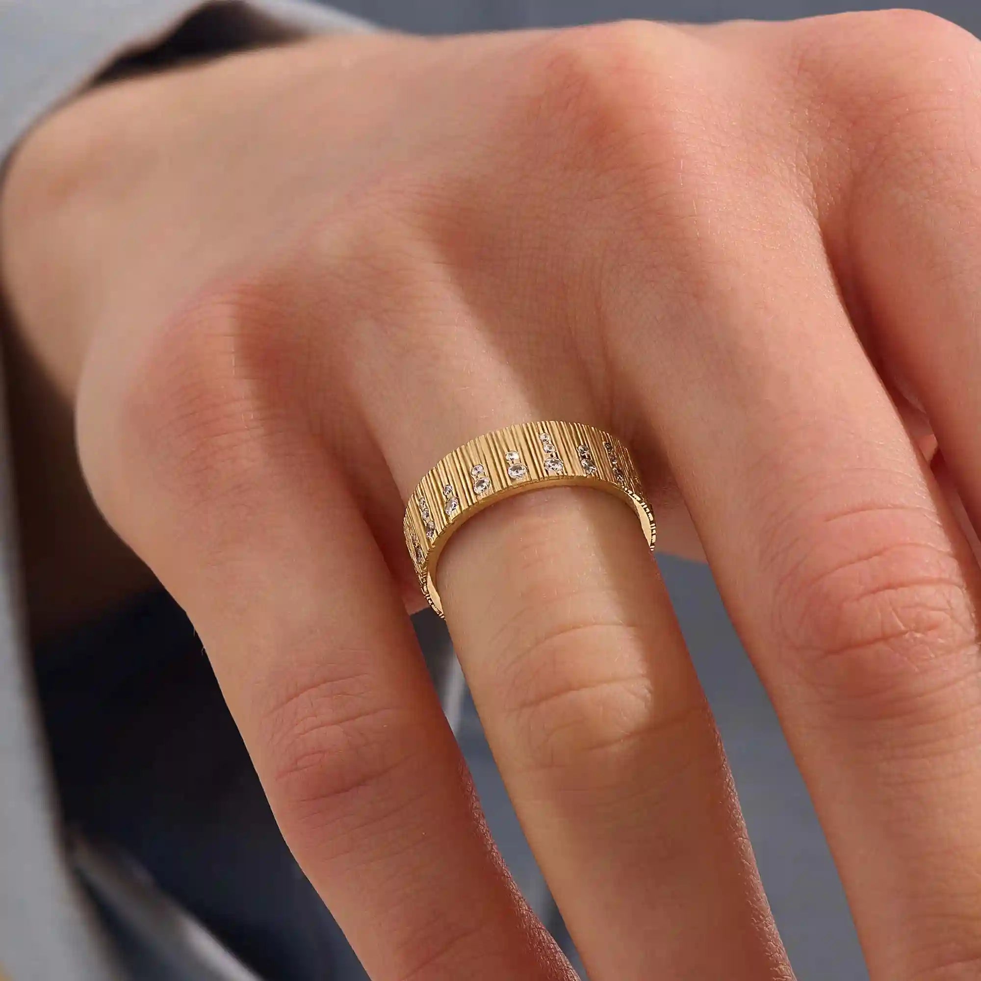Close-up of a woman wearing a 14k solid yellow gold wide wedding band with wood grain texture and pavé set round brilliant cut moissanite stones, distinctive and modern statement jewelry