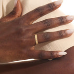 Close-up of a woman wearing a 14k solid yellow gold wide wedding band with wood grain texture and three bezel set round brilliant cut moissanite stones, distinctive and stylish statement jewelry