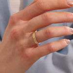 Close-up of a woman wearing a 14k solid yellow gold wide wedding band with wood grain texture and three bezel set round brilliant cut moissanite stones, distinctive and stylish statement jewelry