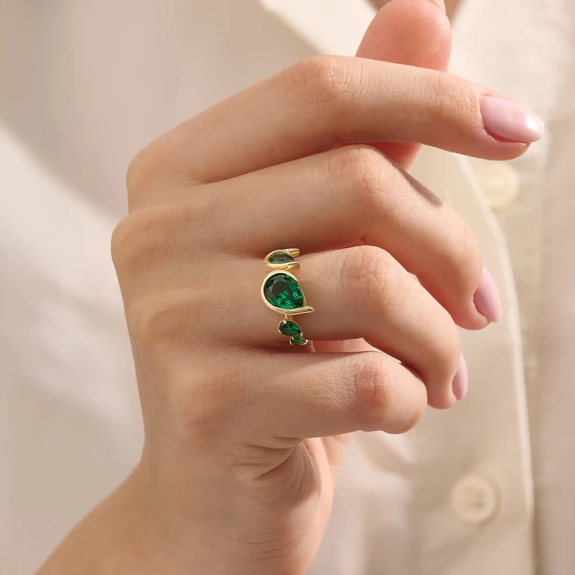 Model showcasing a 14k gold statement ring set with five pear-shaped emeralds. Striking and colorful gemstone ring perfect for standout looks.