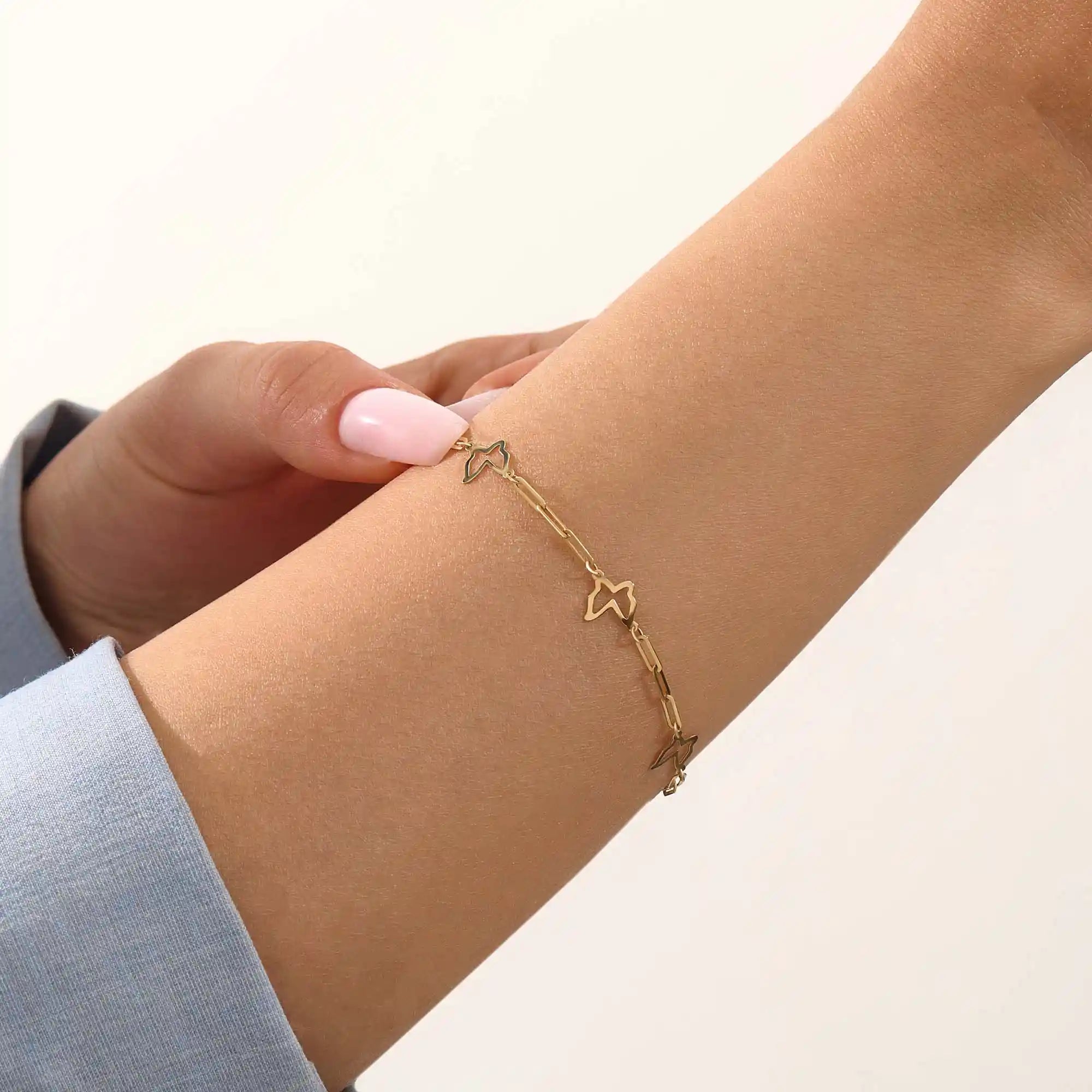 Model wearing a 14k gold butterfly bracelet with open butterfly charms and lightweight chain design.