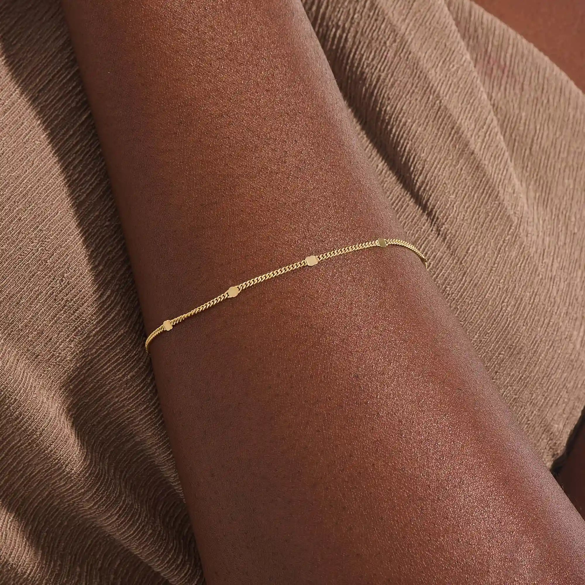 Model wearing a 14k gold chain bracelet with curb links and disc accents, modern and stylish.