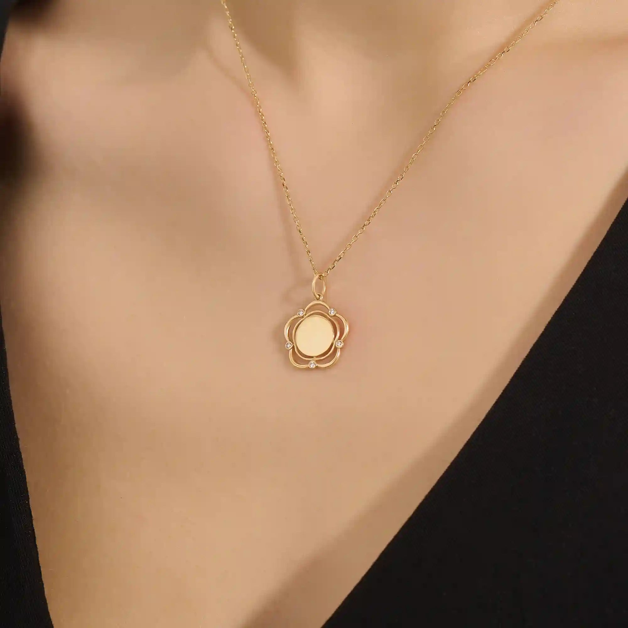 Model wearing a 14k gold flower pendant necklace with an engravable plain surface. A delicate and personalized accessory ideal for daily wear.