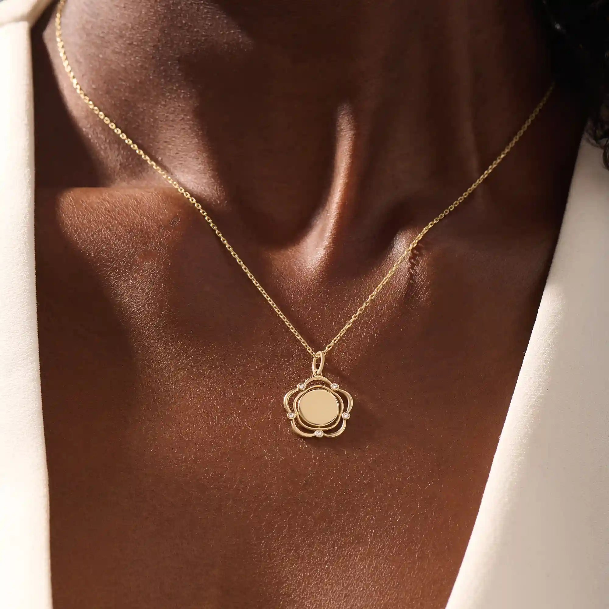 Model wearing a 14k gold flower pendant necklace with an engravable plain surface. A delicate and personalized accessory ideal for daily wear.