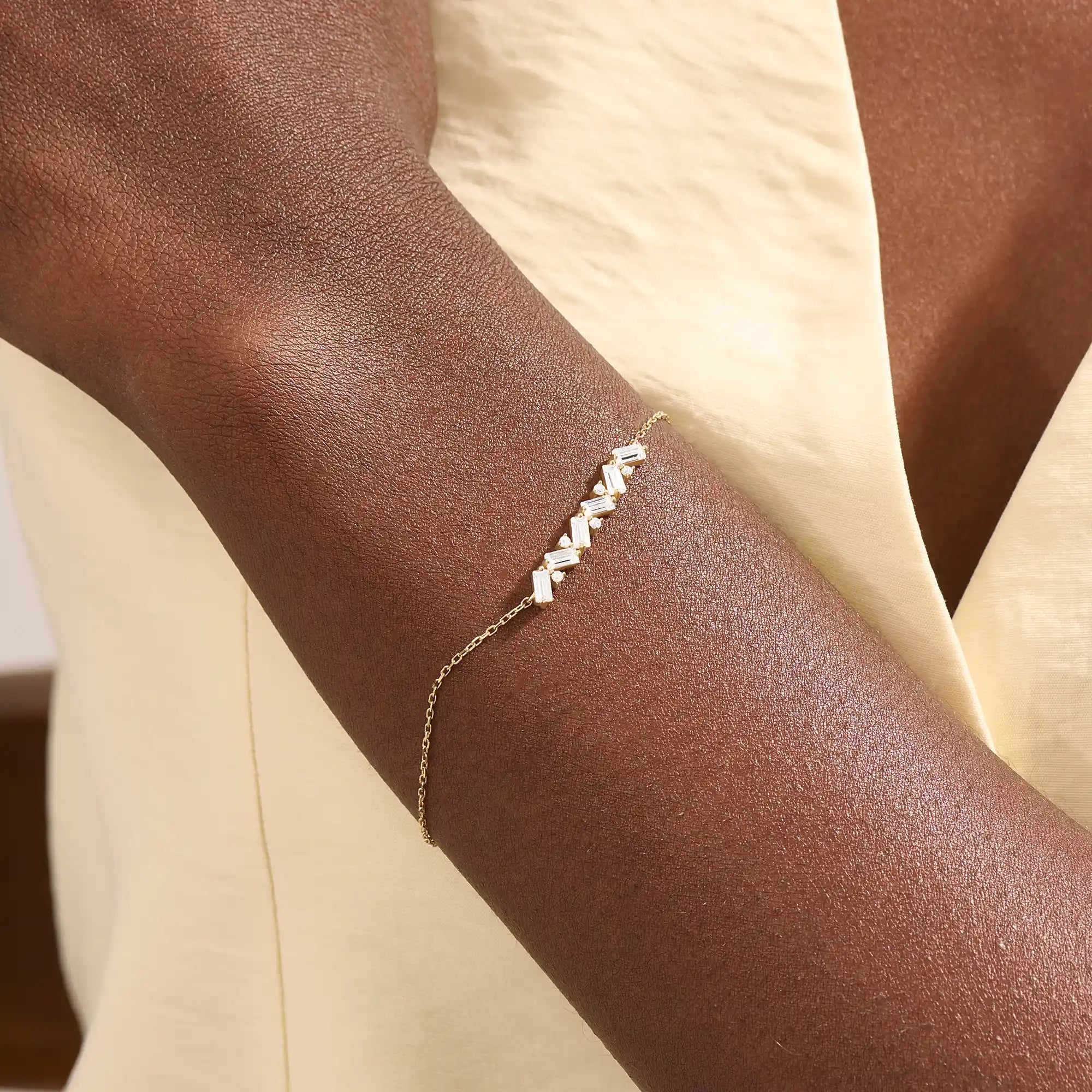 Model wearing a 14k yellow gold baguette bar bracelet with baguette-cut and round stones, adding sparkle to a refined wrist look.