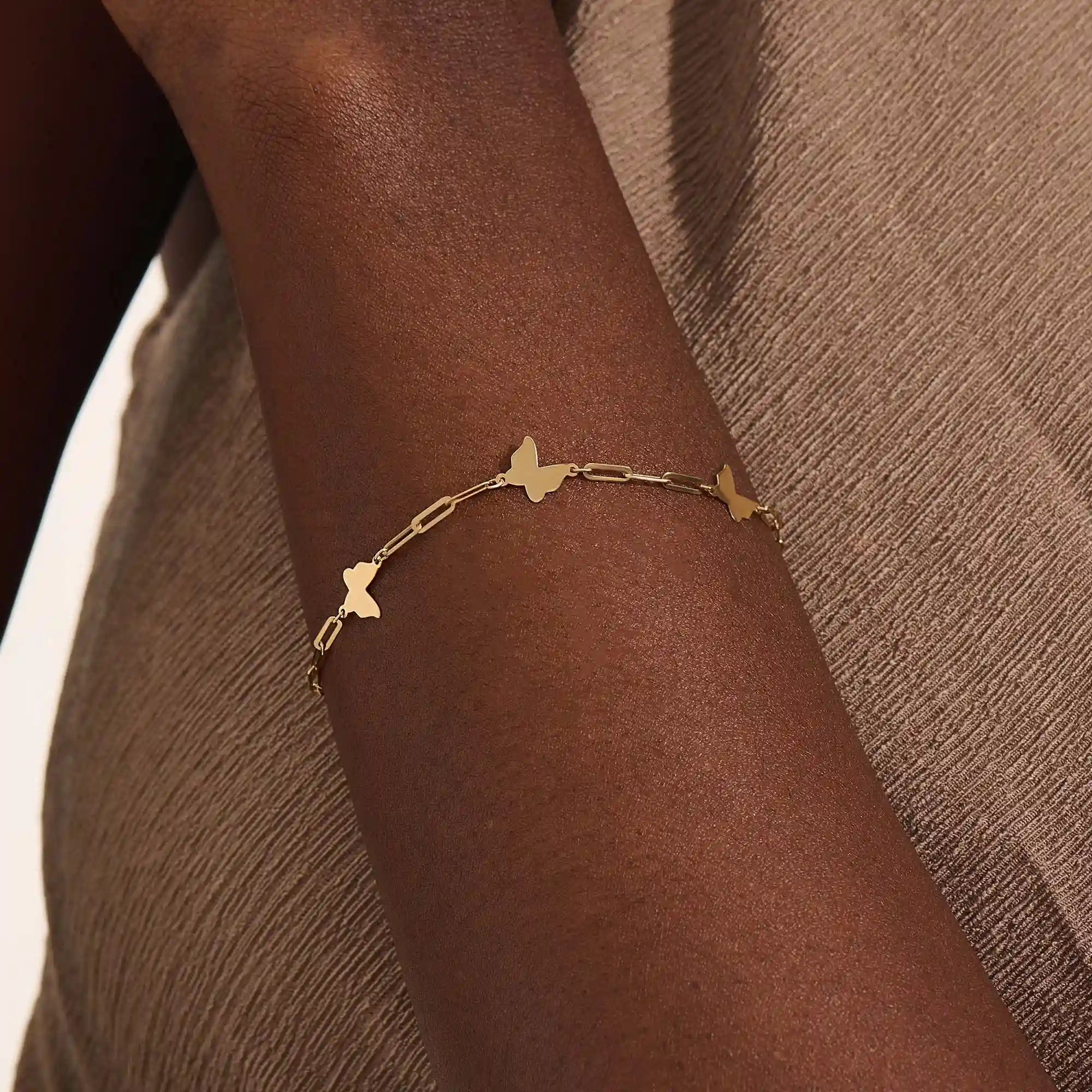 Model wearing a 14k yellow gold butterfly chain bracelet with polished butterfly charms and delicate chain details.