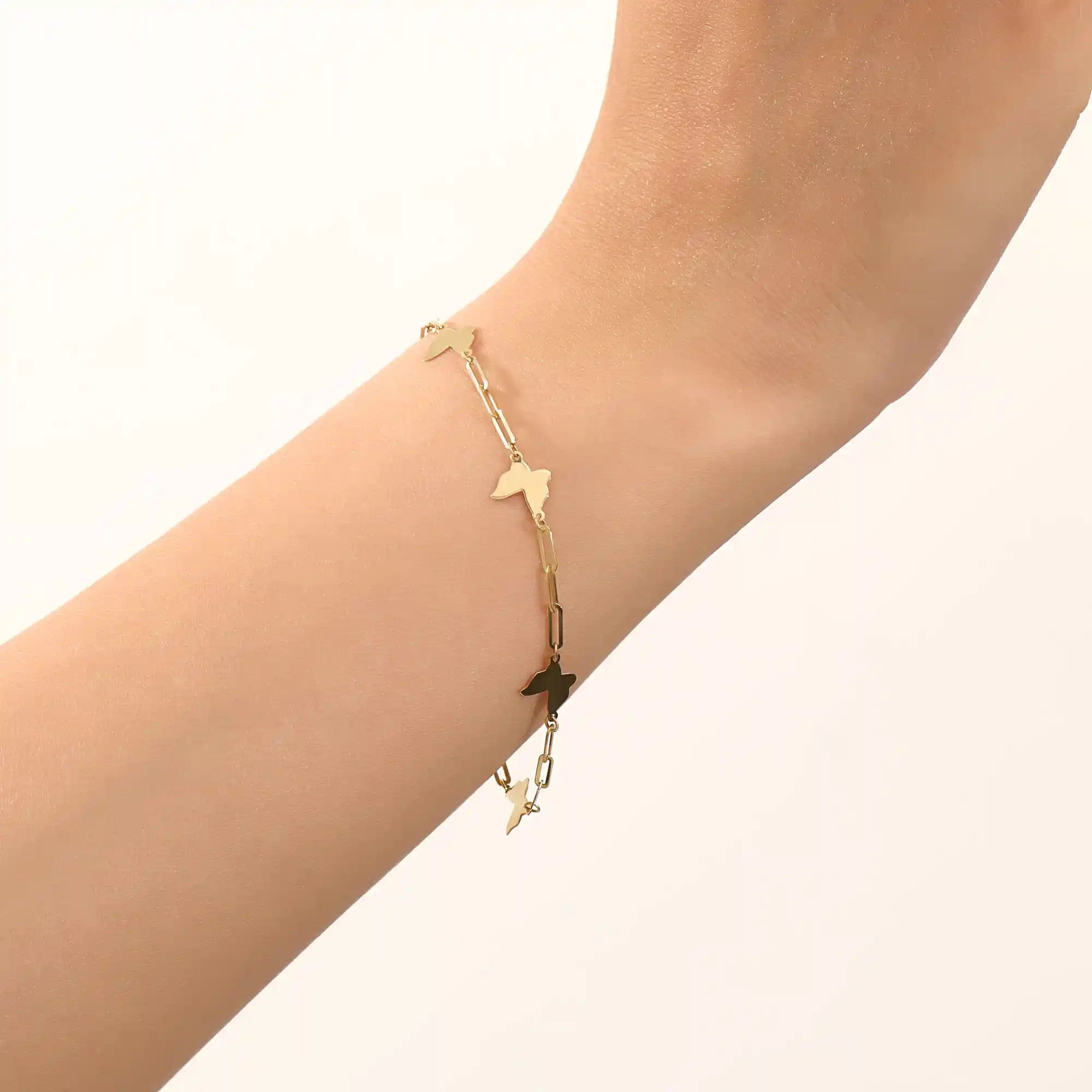 Model wearing a 14k yellow gold butterfly chain bracelet with polished butterfly charms and delicate chain details.