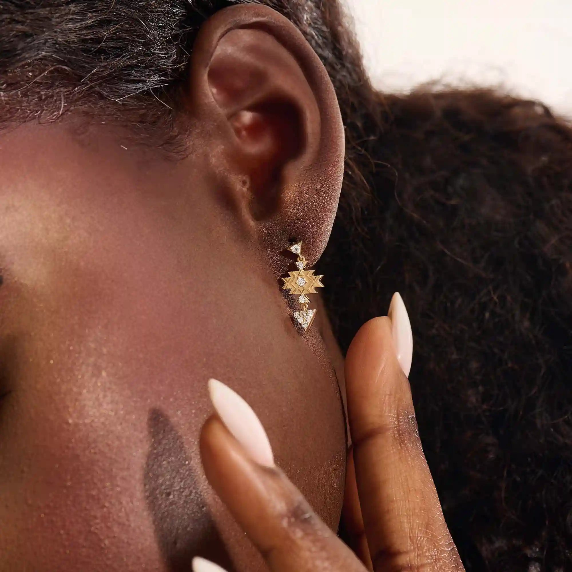Model wearing dangling motif stud earrings in 14k gold, featuring moissanite-accented geometric star and triangle designs.