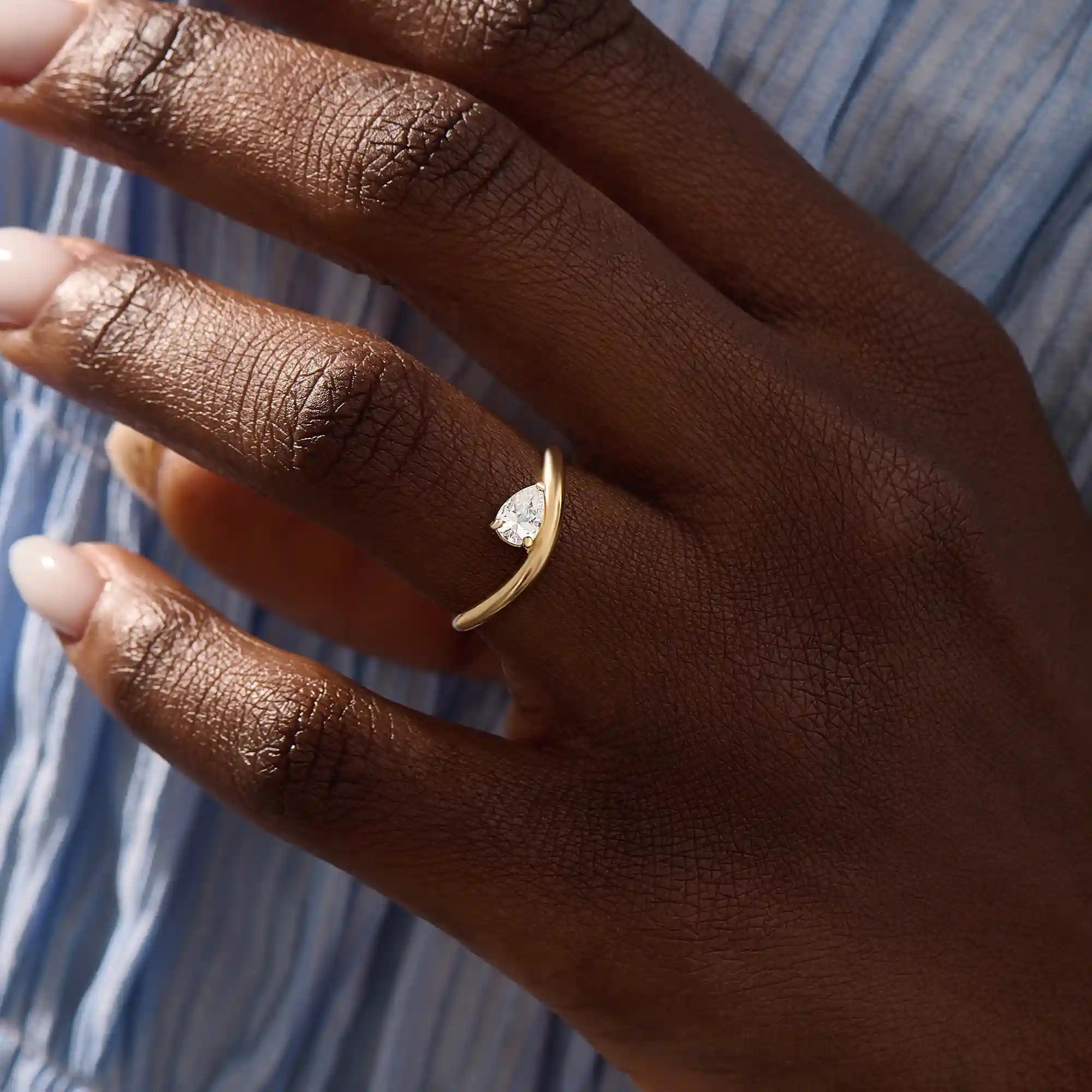 Model wearing pear cut moissanite solitaire engagement ring on a curved 14k solid gold band, highlighting its sleek and modern minimalist style.