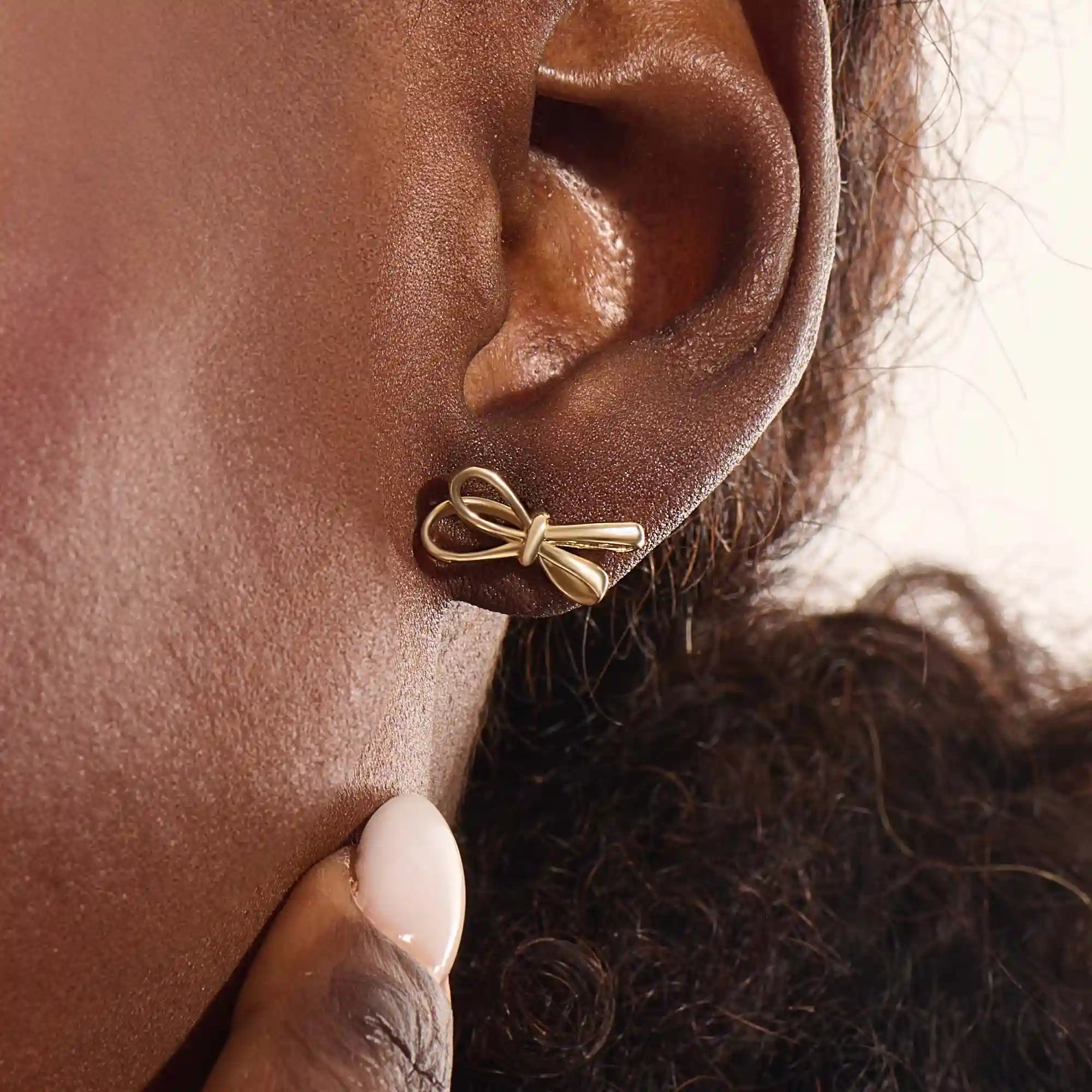 Model wearing simple ribbon stud earrings in 14k gold, showcasing their playful and elegant bow style.