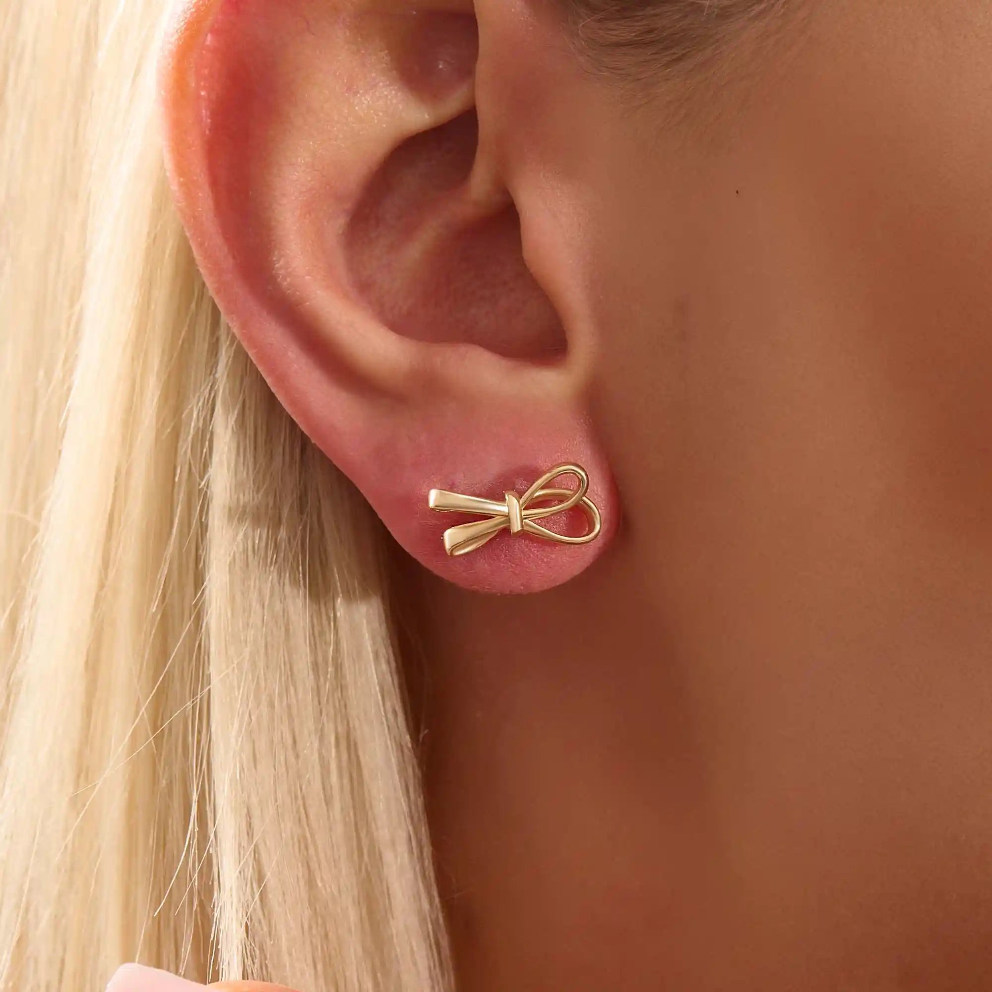 Model wearing simple ribbon stud earrings in 14k gold, showcasing their playful and elegant bow style.