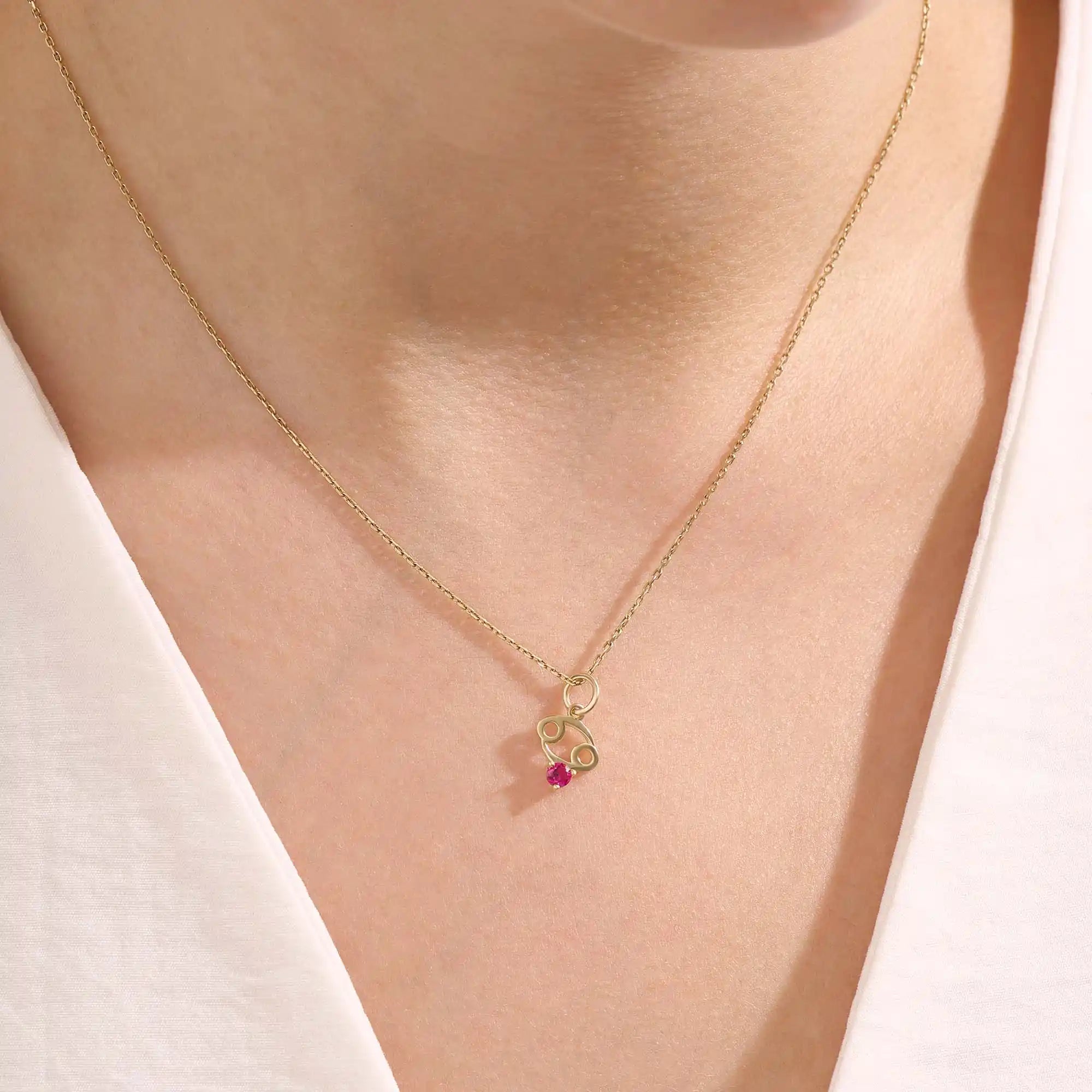 Model wears a 14k gold Cancer symbol necklace with a ruby accent. Elegant and symbolic, perfect for everyday wear or gifting.