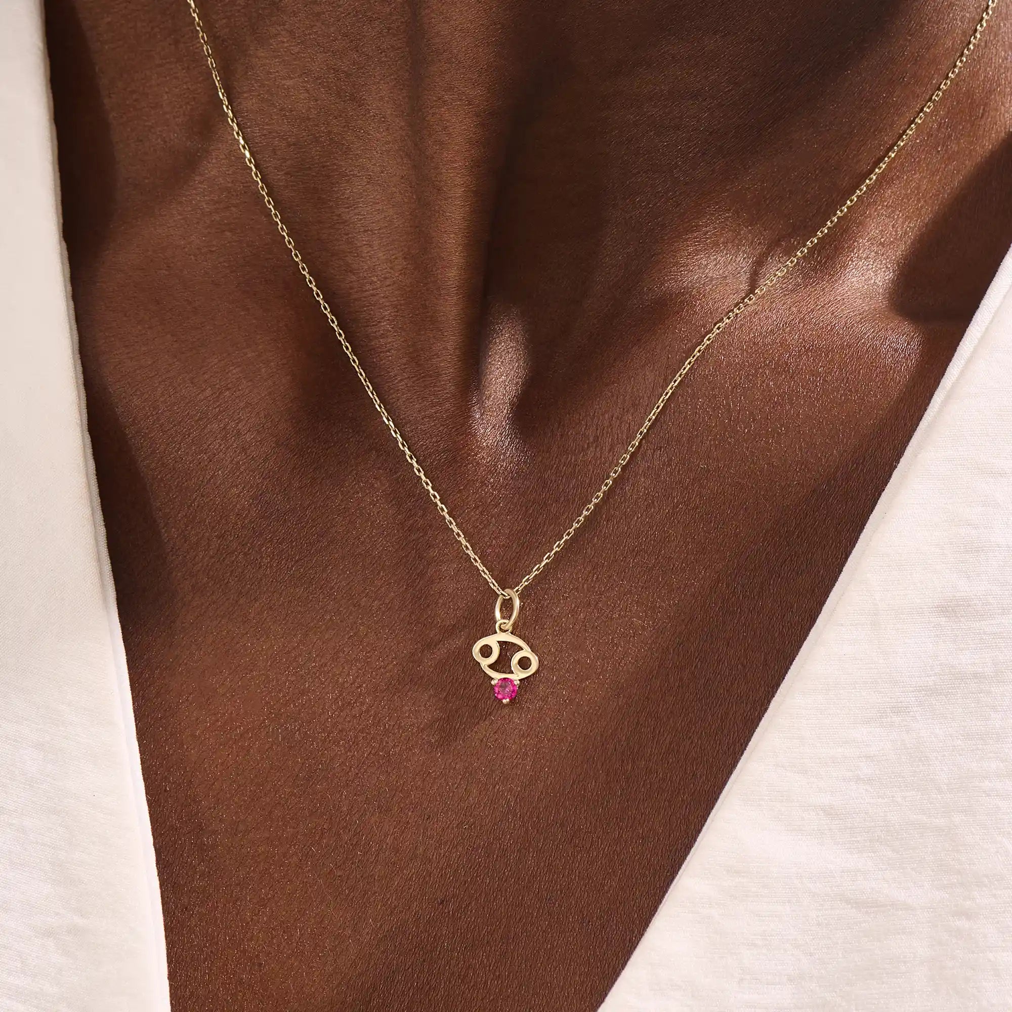 Model wears a 14k gold Cancer symbol necklace with a ruby accent. Elegant and symbolic, perfect for everyday wear or gifting.
