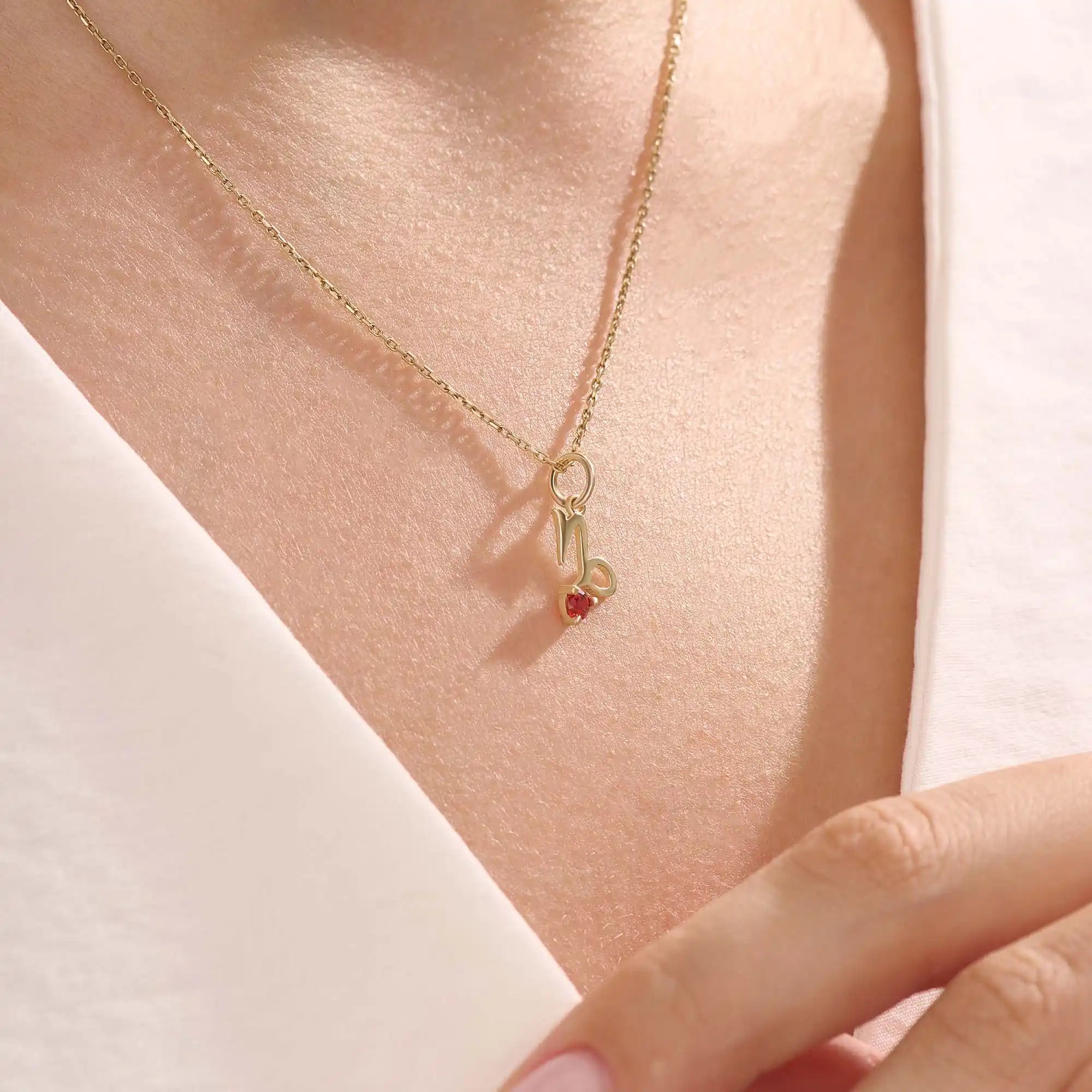 Model wears a 14k gold Capricorn zodiac necklace with a garnet birthstone accent. Elegant and symbolic jewelry for daily wear.