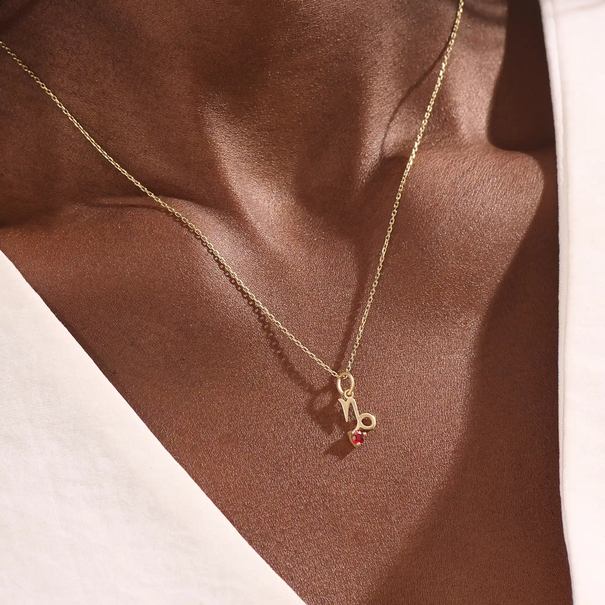 Model wears a 14k gold Capricorn zodiac necklace with a garnet birthstone accent. Elegant and symbolic jewelry for daily wear.
