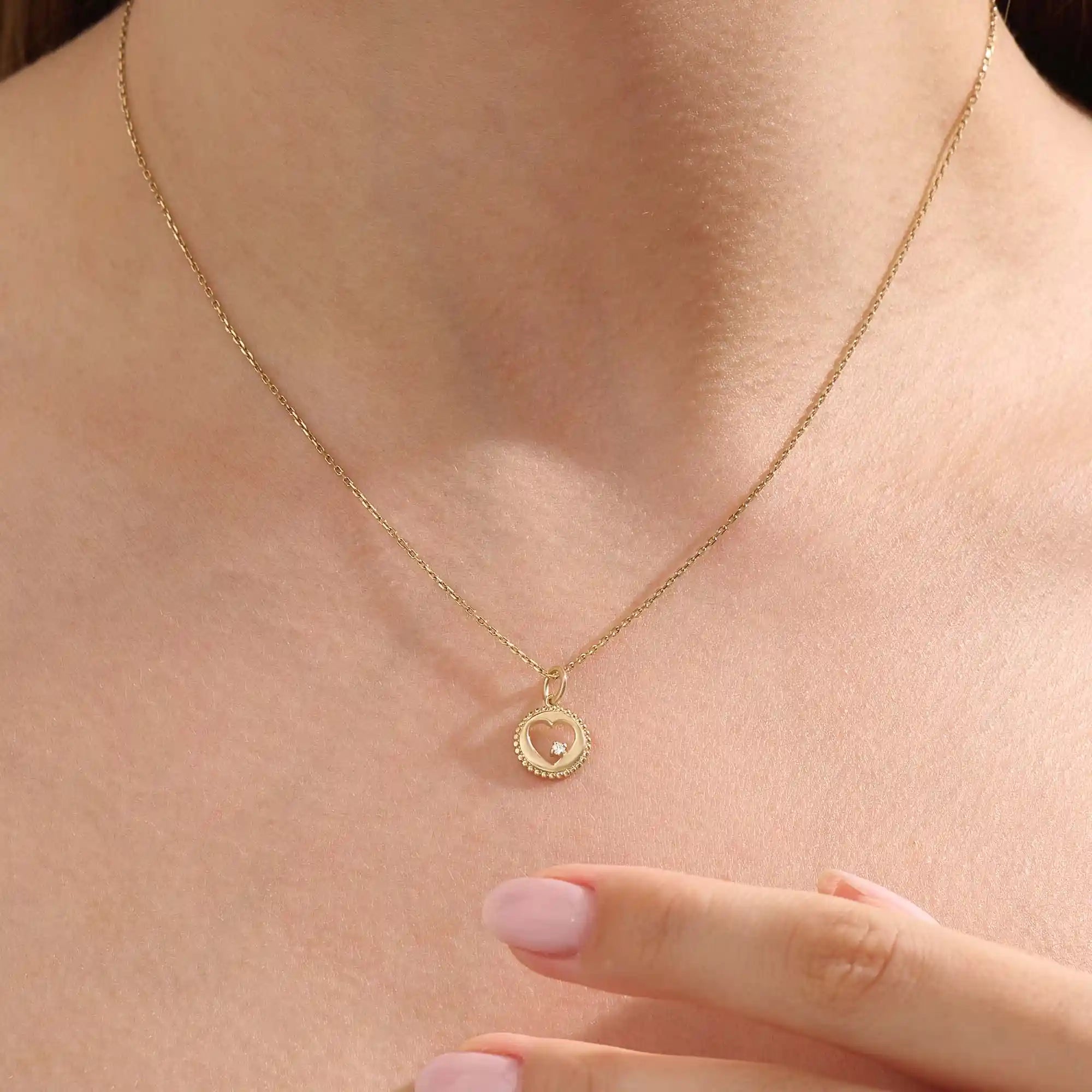 Model wears a 14k gold circle pendant necklace with a heart cutout and single moissanite accent. A minimalist and elegant everyday piece.