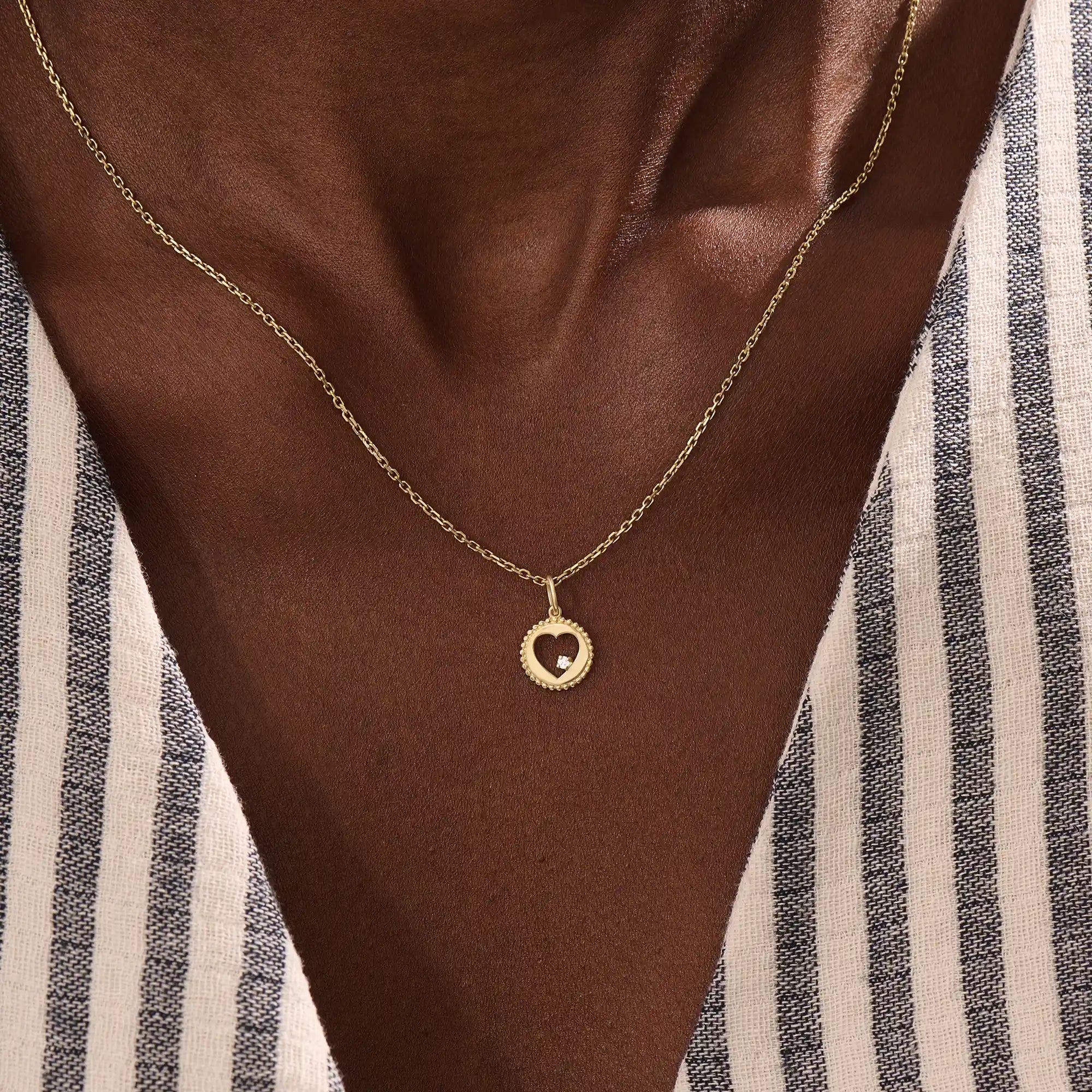 Model wears a 14k gold circle pendant necklace with a heart cutout and single moissanite accent. A minimalist and elegant everyday piece.