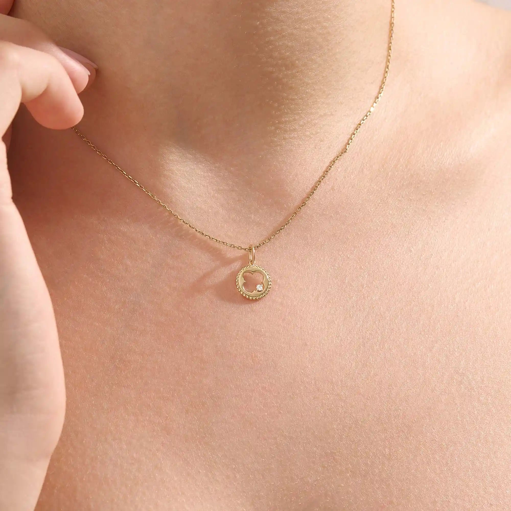 Model wears a 14k gold circle pendant necklace with clover cutout and single moissanite accent. A minimalist and meaningful everyday accessory.