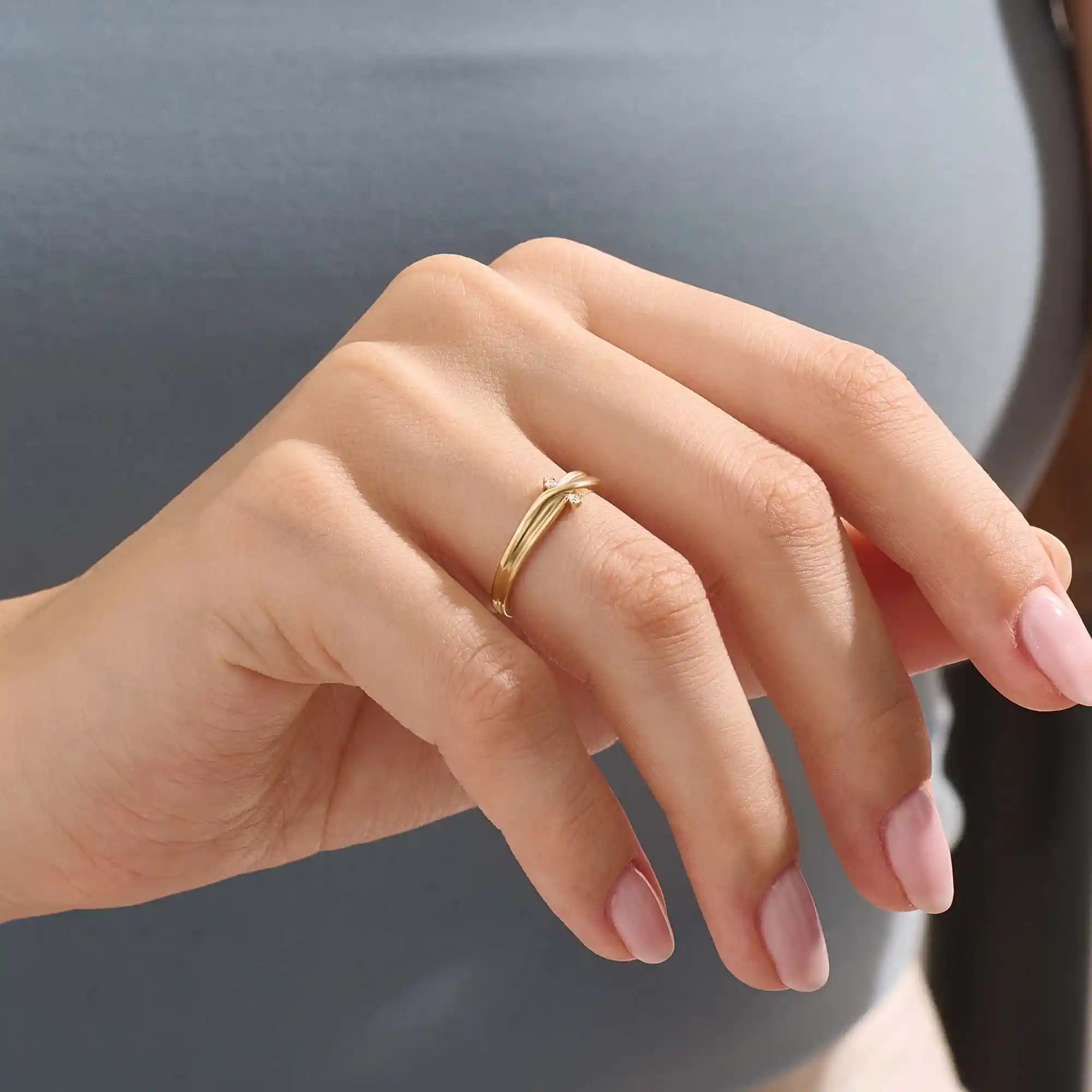Model wears a 14k gold crossover band promise ring featuring delicate moissanite accents. A stylish and modern symbol of commitment.