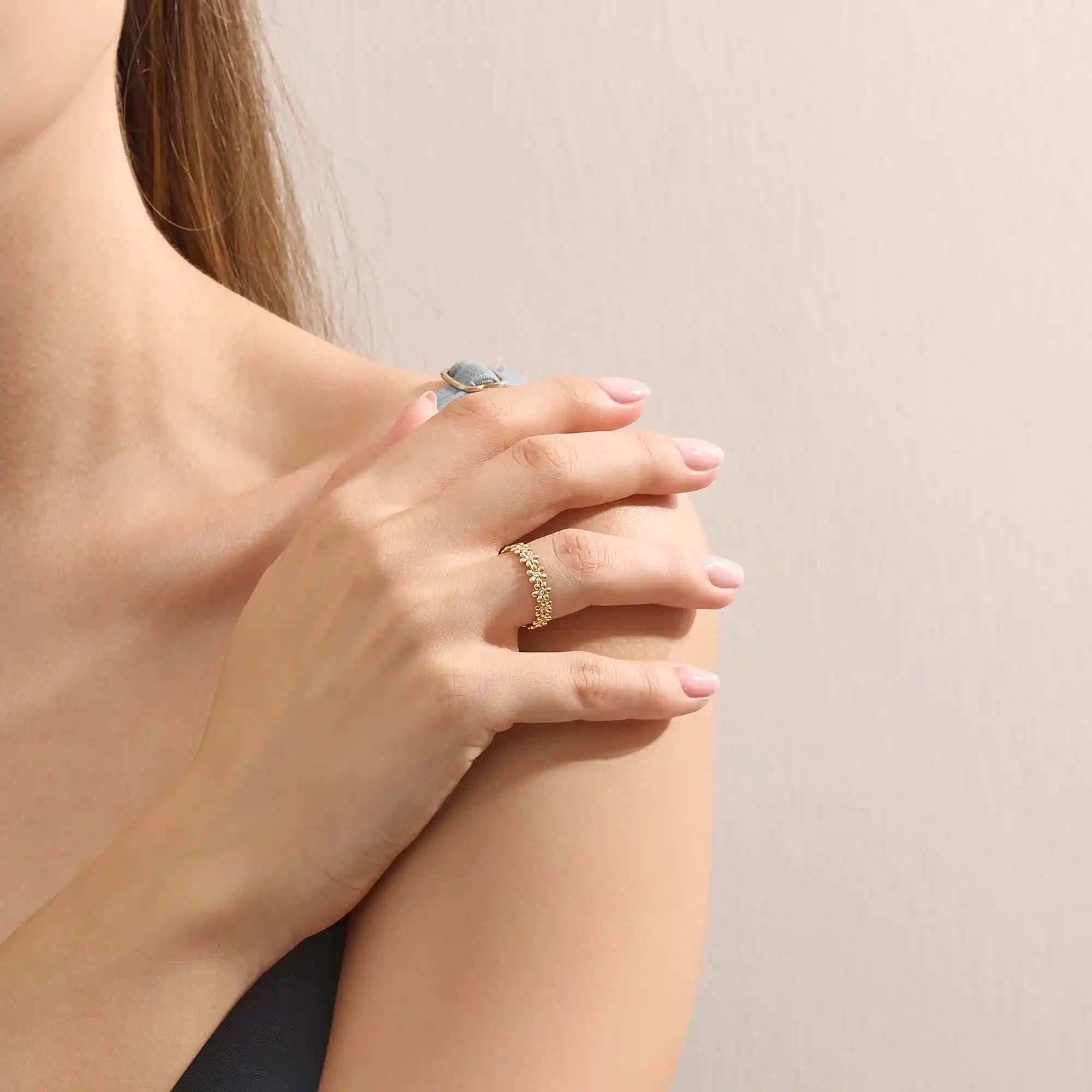 Model wears a 14k gold eternity band ring featuring small daisy flowers. Perfect for stacking or as a charming everyday statement piece