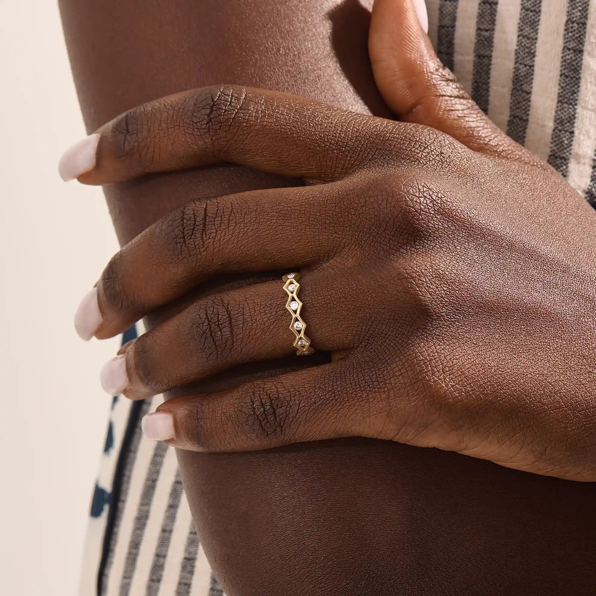 Model wears a 14k gold eternity band ring with geometric rhombus shapes and moissanite accents. A striking and contemporary statement piece.