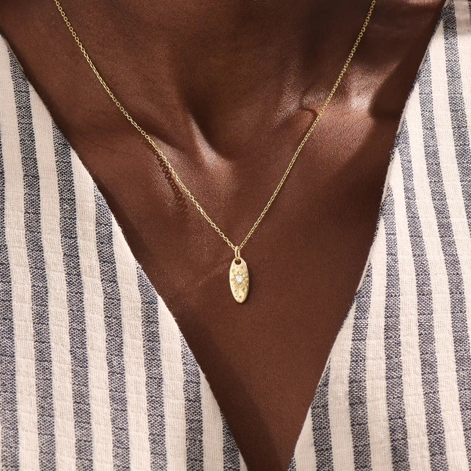 Model wears a 14k gold oval celestial pendant necklace with moissanite Northstar detail. A refined and meaningful accessory for everyday wear.