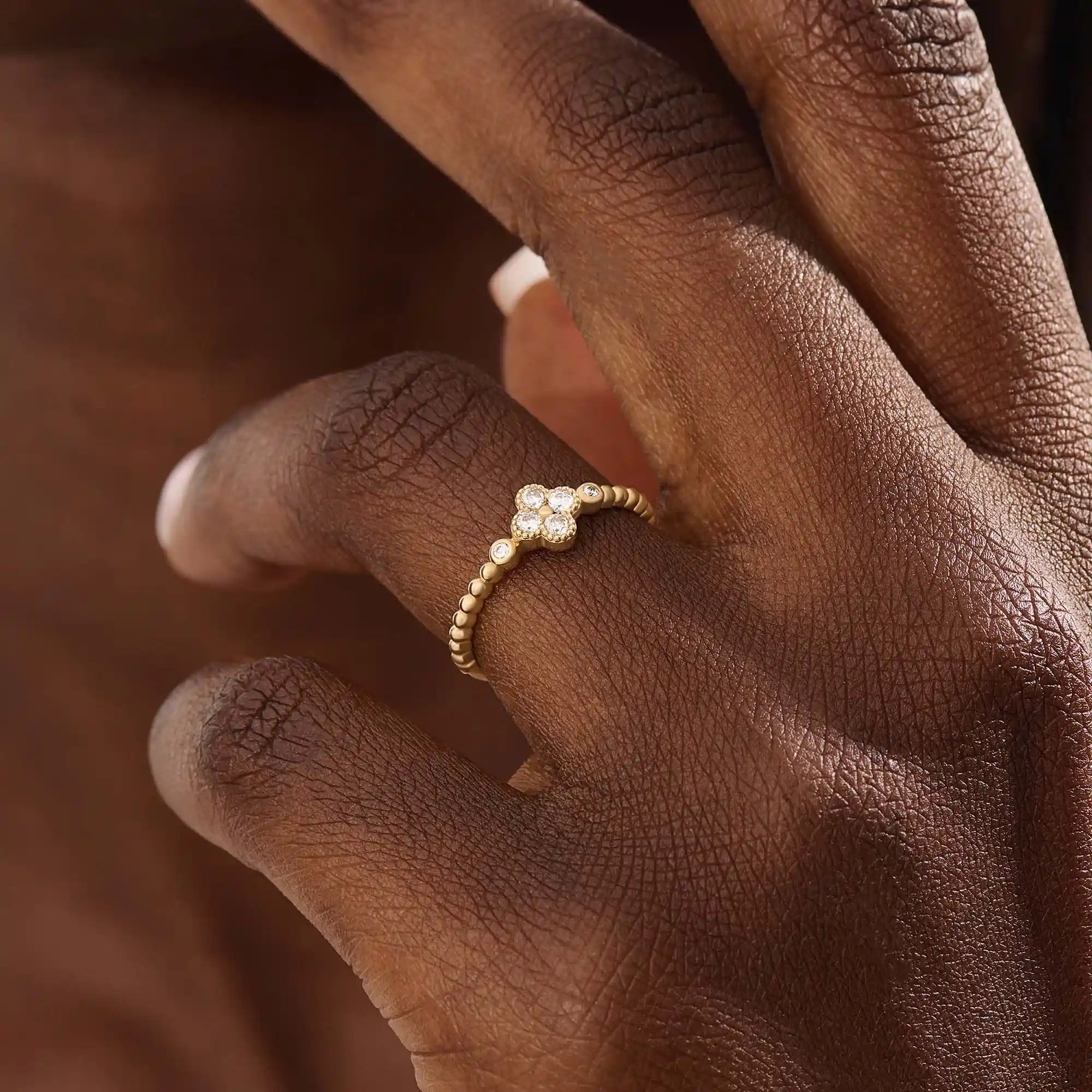 Model wears a 14k gold pinky signet ring featuring a clover-shaped moissanite and textured beaded band. Elegant and meaningful everyday jewelry.