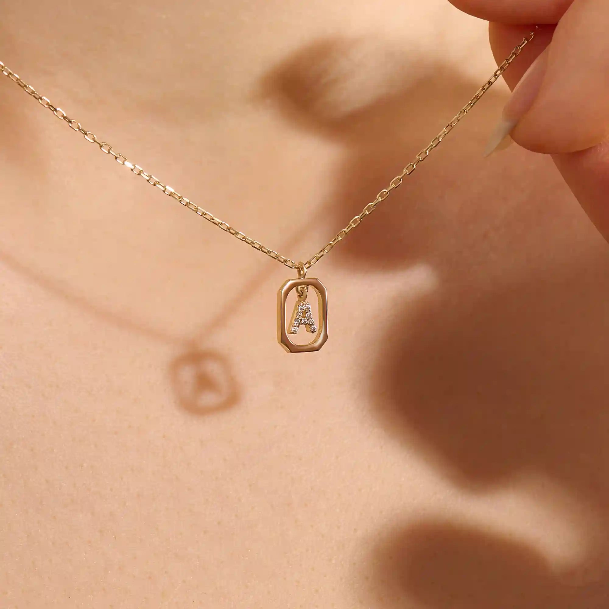 Model wears a 14k gold rectangle necklace with a dangling personalized letter charm. Sleek and meaningful jewelry perfect for layering.