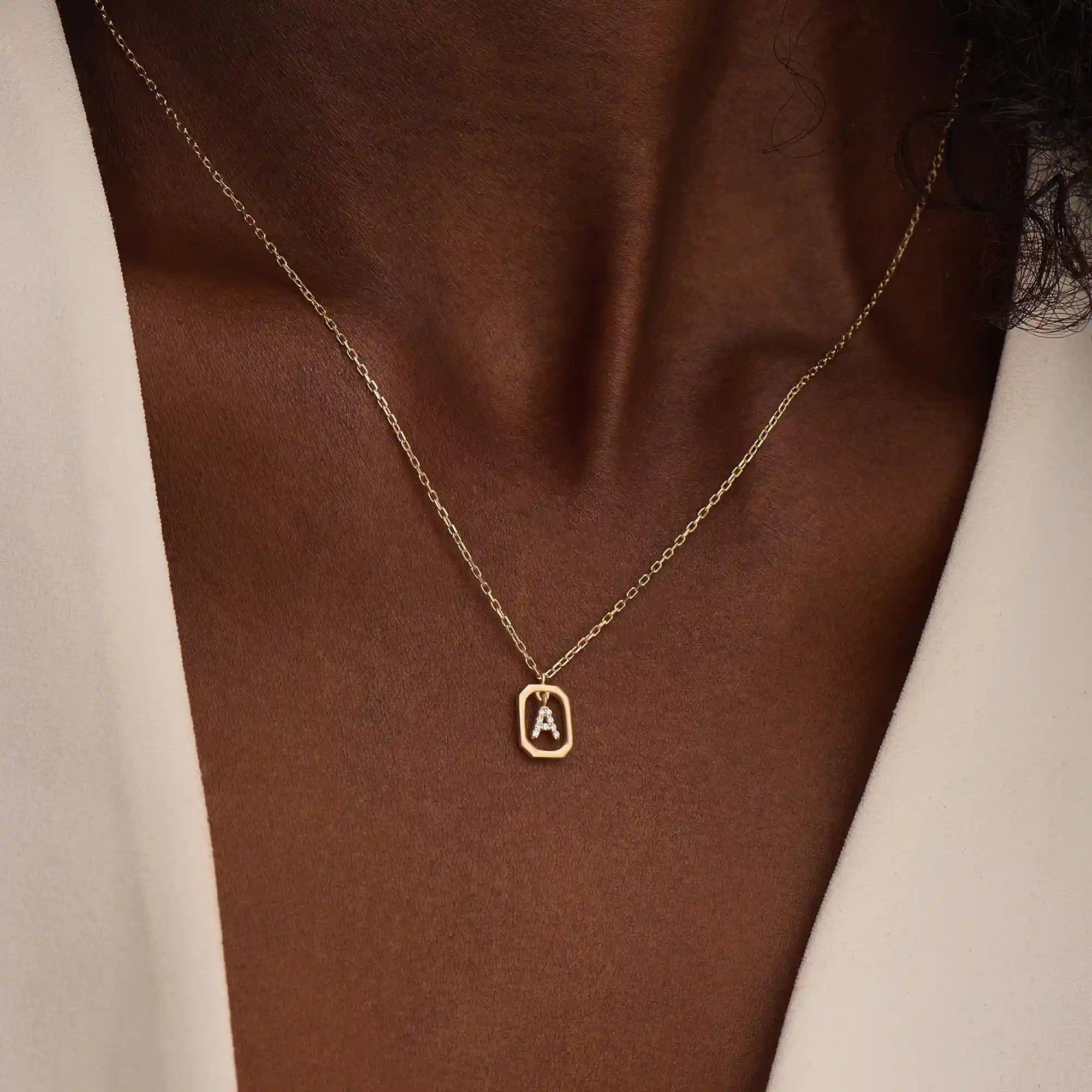 Model wears a 14k gold rectangle necklace with a dangling personalized letter charm. Sleek and meaningful jewelry perfect for layering.