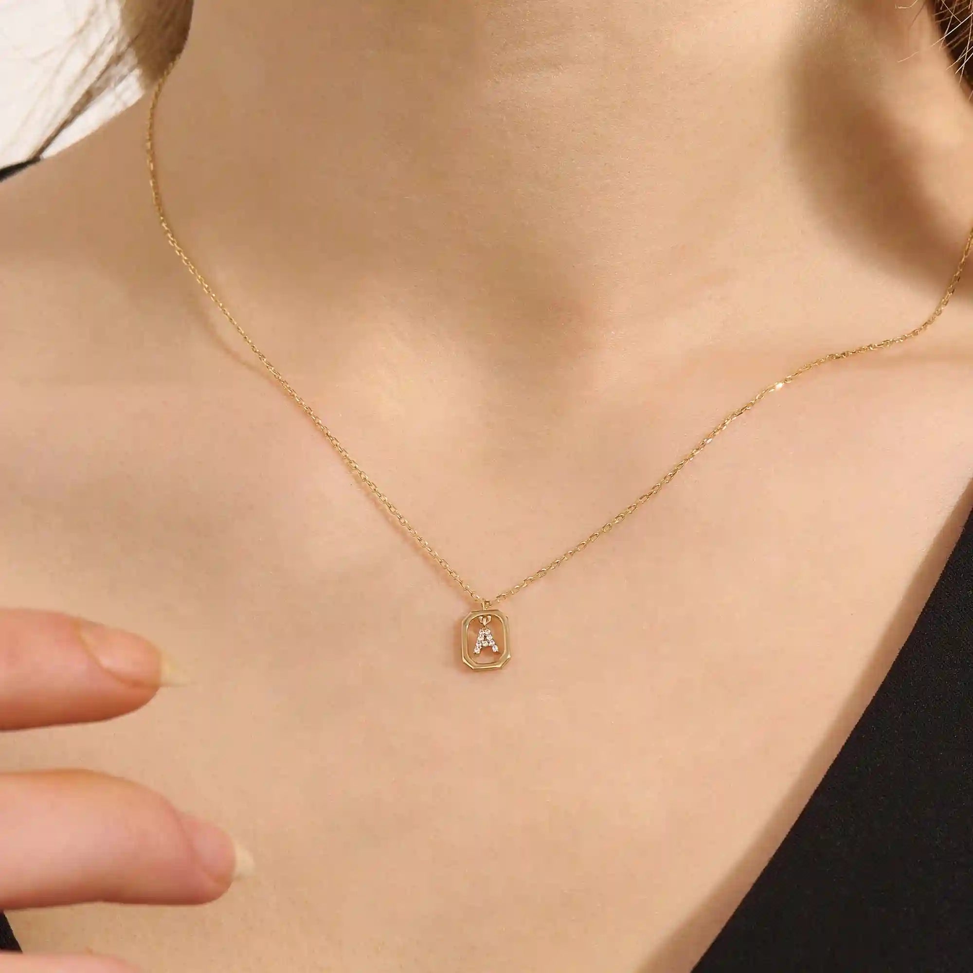 Model wears a 14k gold rectangle necklace with a dangling personalized letter charm. Sleek and meaningful jewelry perfect for layering.