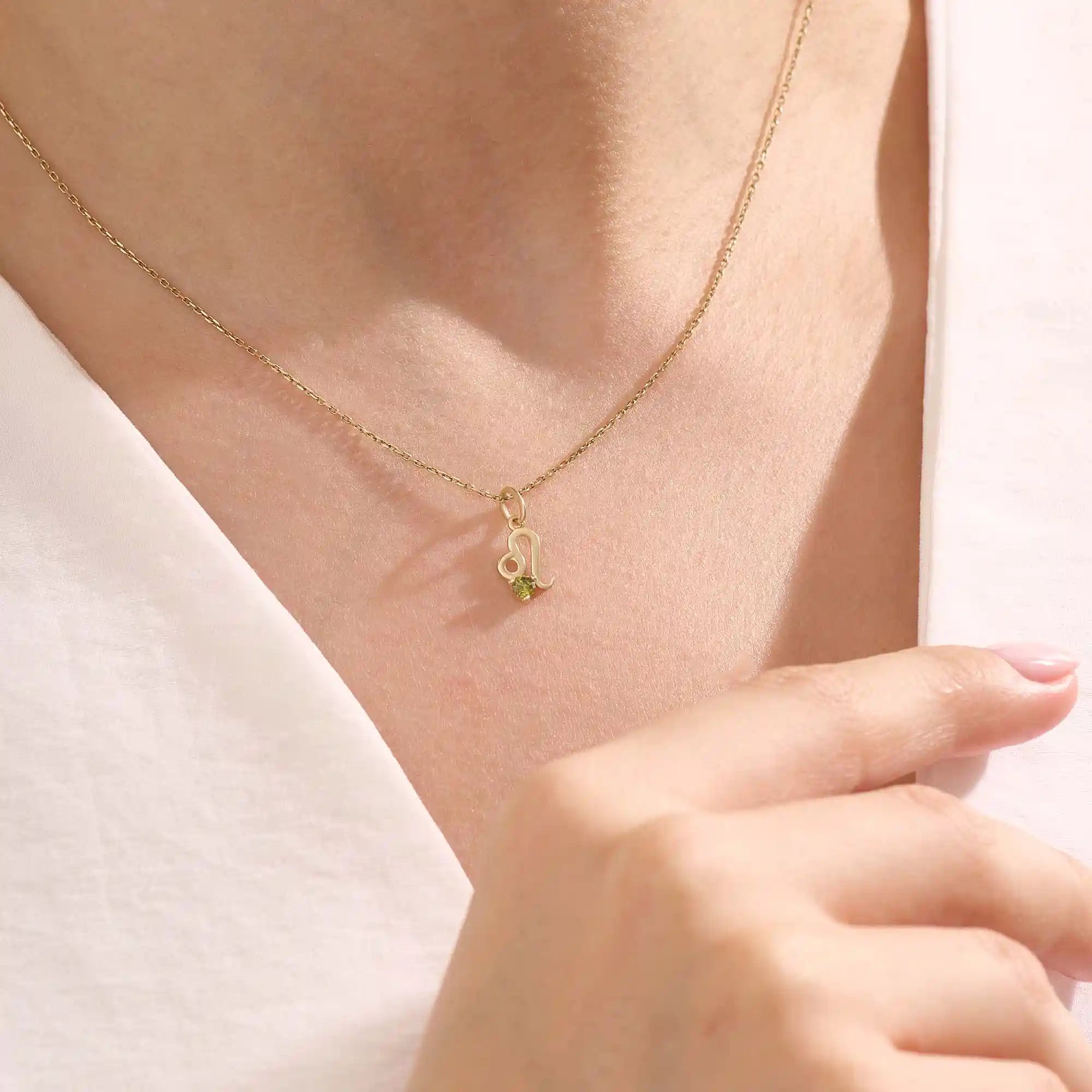 Model wears a 14k solid gold Leo zodiac symbol pendant necklace with green peridot, perfect for Leo zodiac birthdays.