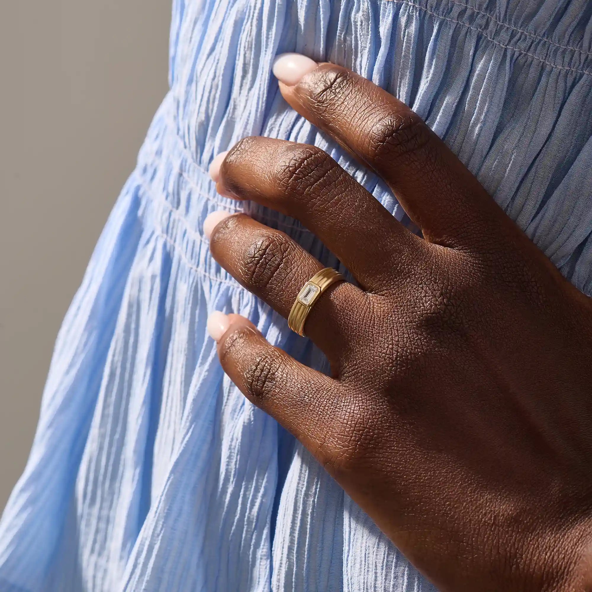 Model wears a 14k solid gold chunky engagement ring with a thick band and bezel-set emerald-cut moissanites. Elegant and bold statement piece for modern brides.