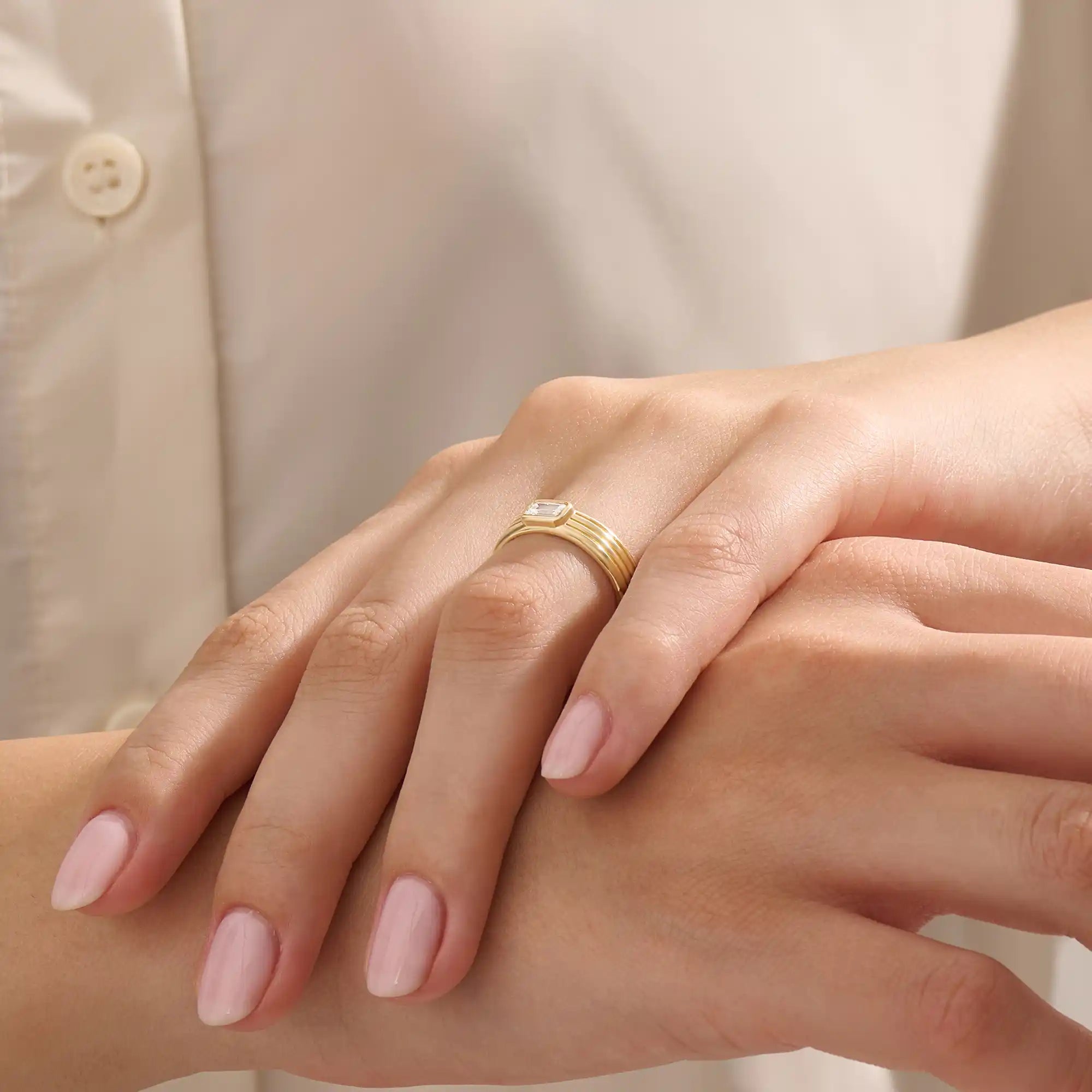 Model wears a 14k solid gold chunky engagement ring with a thick band and bezel-set emerald-cut moissanites. Elegant and bold statement piece for modern brides.