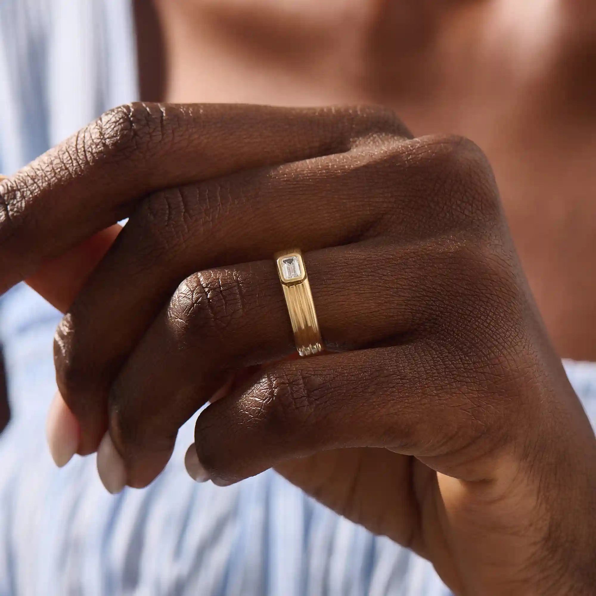 Model wears a 14k solid gold chunky engagement ring with a thick band and bezel-set emerald-cut moissanites. Elegant and bold statement piece for modern brides.