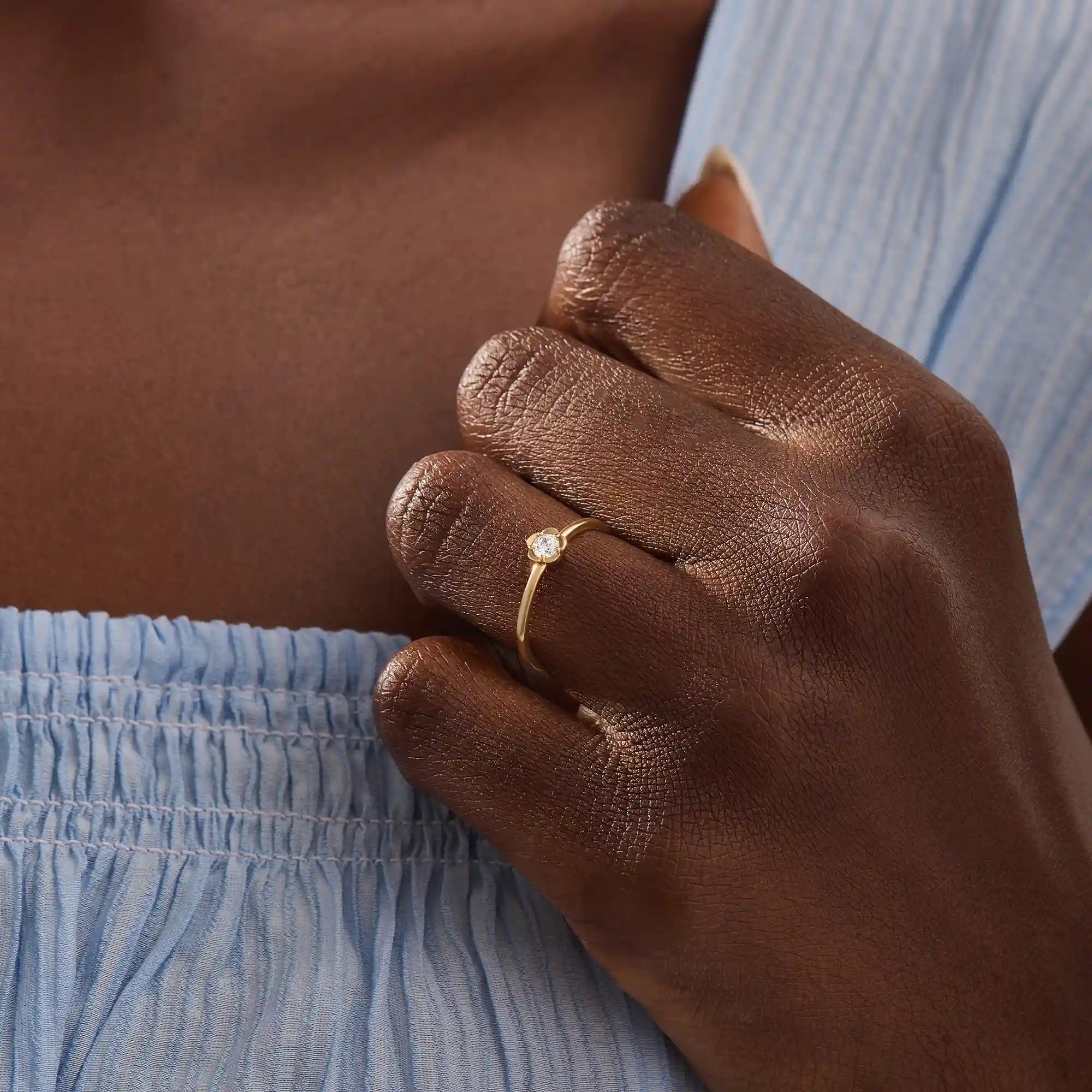 Model wears a 14k solid gold solitaire engagement or promise ring with a small flower motif. Elegant and subtle design for women’s daily wear or special occasions.