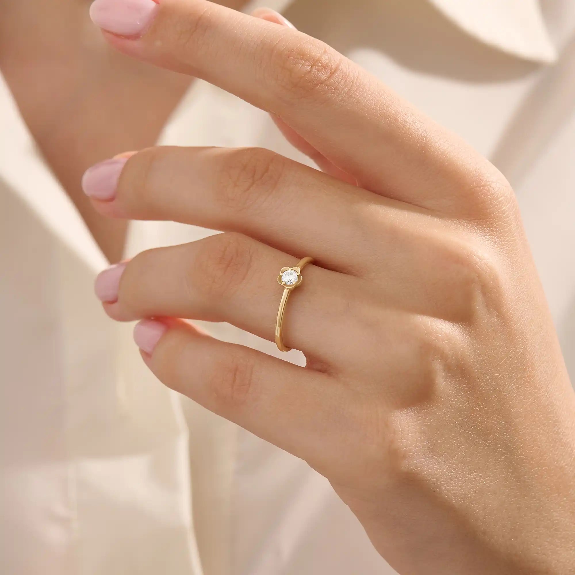 Model wears a 14k solid gold solitaire engagement or promise ring with a small flower motif. Elegant and subtle design for women’s daily wear or special occasions.