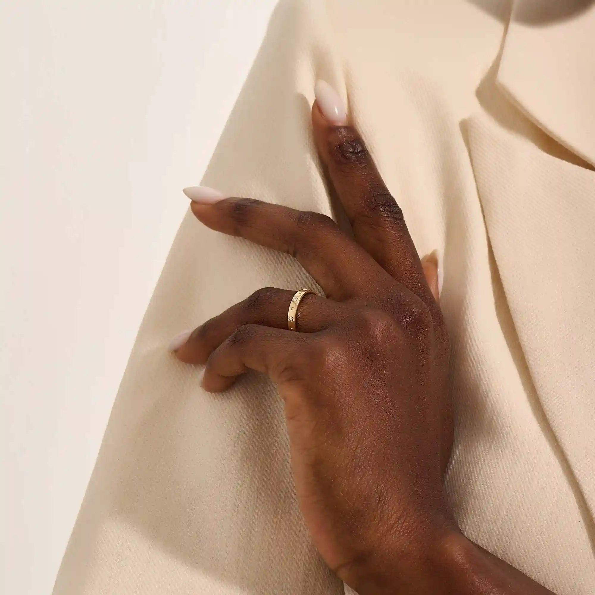 Close-up of a woman wearing a 14k solid yellow gold wedding band decorated with tiny moissanite-set star motifs, styled alone for an understated yet whimsical celestial look.