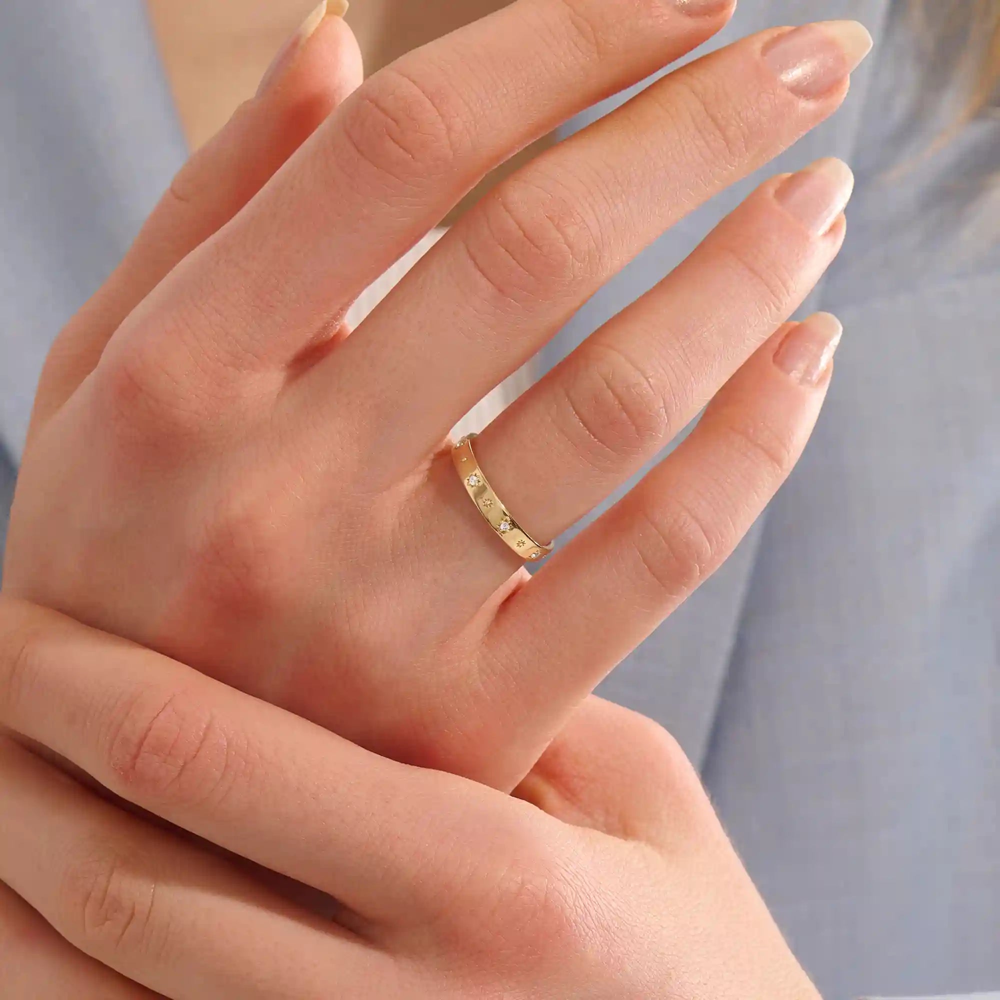 Close-up of a woman wearing a 14k solid yellow gold wedding band decorated with tiny moissanite-set star motifs, styled alone for an understated yet whimsical celestial look.