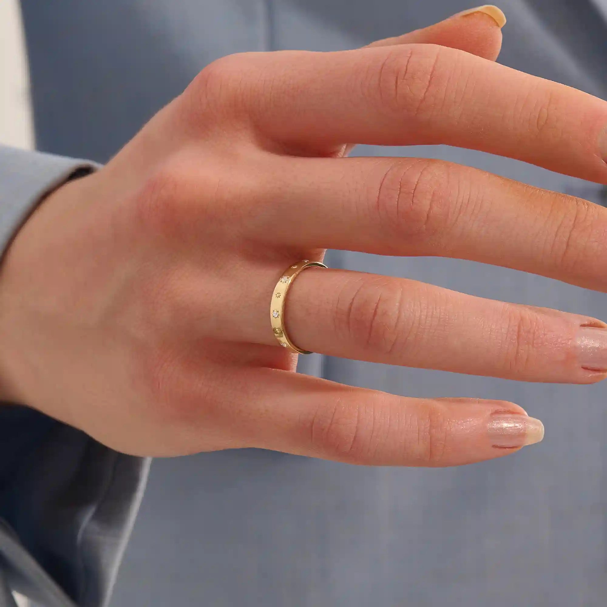 Close-up of a woman wearing a 14k solid yellow gold wedding band decorated with tiny moissanite-set star motifs, styled alone for an understated yet whimsical celestial look.