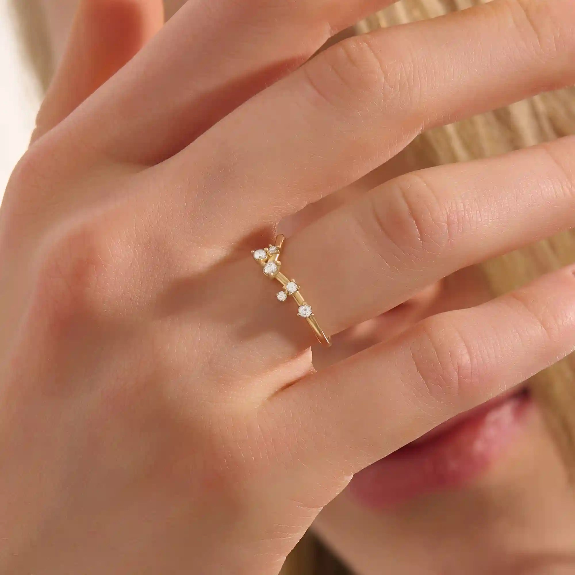 Model wears a curved 14k gold nesting ring with scattered moissanites. A delicate stacking piece that adds soft brilliance to any ring stack.