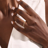 Model wears a dainty curved 14k gold ring featuring a twisted band detail. Ideal as a nesting ring or part of a minimalist stack.