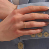 Model wears a dainty curved 14k gold ring featuring a twisted band detail. Ideal as a nesting ring or part of a minimalist stack.