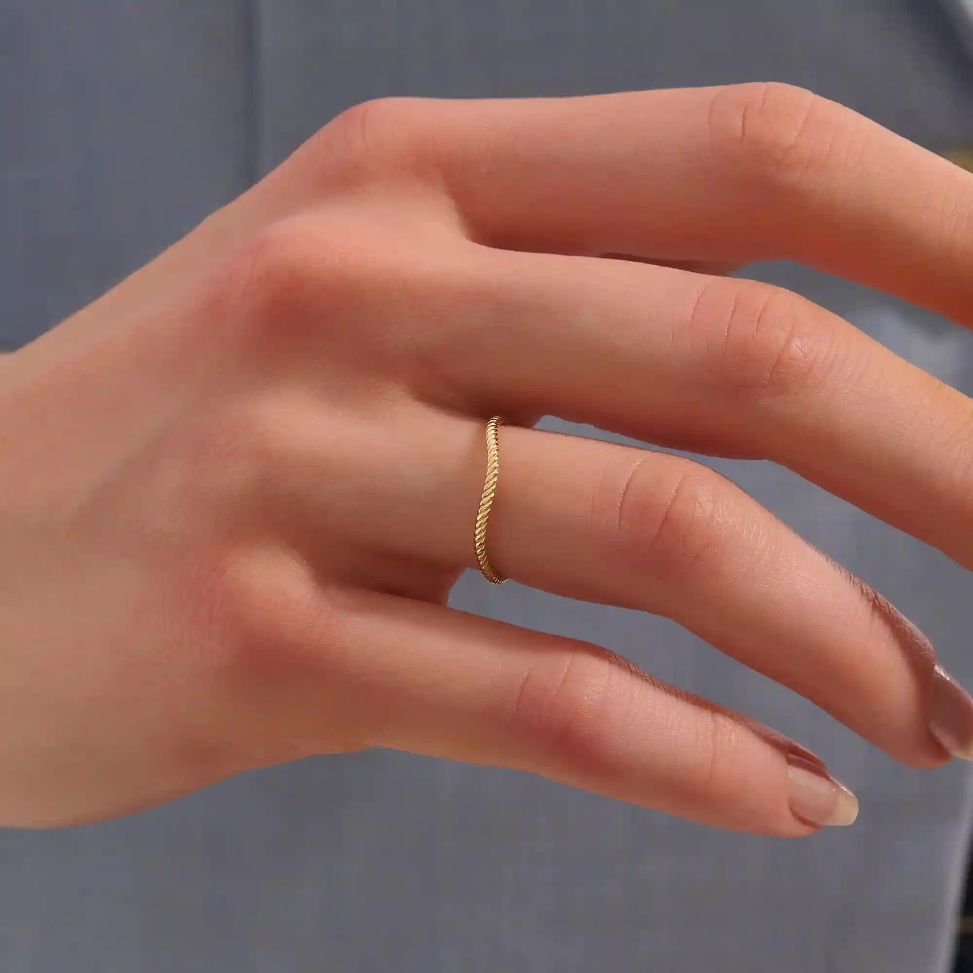 Model wears a dainty curved 14k gold ring featuring a twisted band detail. Ideal as a nesting ring or part of a minimalist stack.