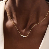 Model wears a delicate 14k gold necklace with three bezel-set moissanites. Elegant and versatile, ideal for stacking with other necklaces.