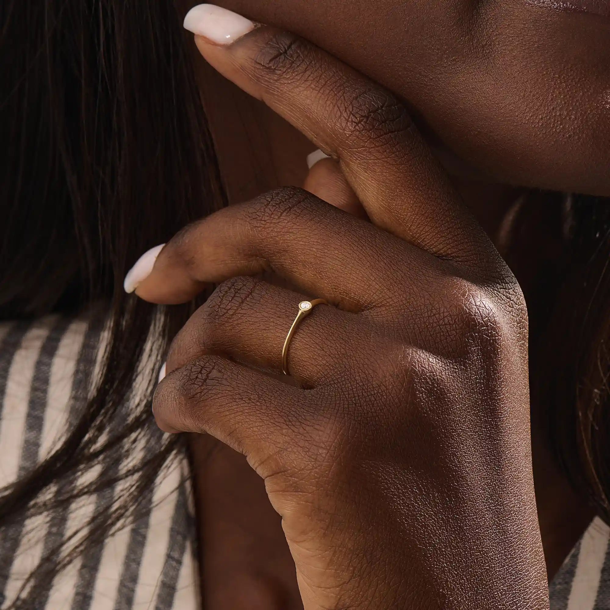 Model wears a simple 14k gold promise ring featuring a small bezel-set moissanite. A subtle and elegant symbol of commitment.