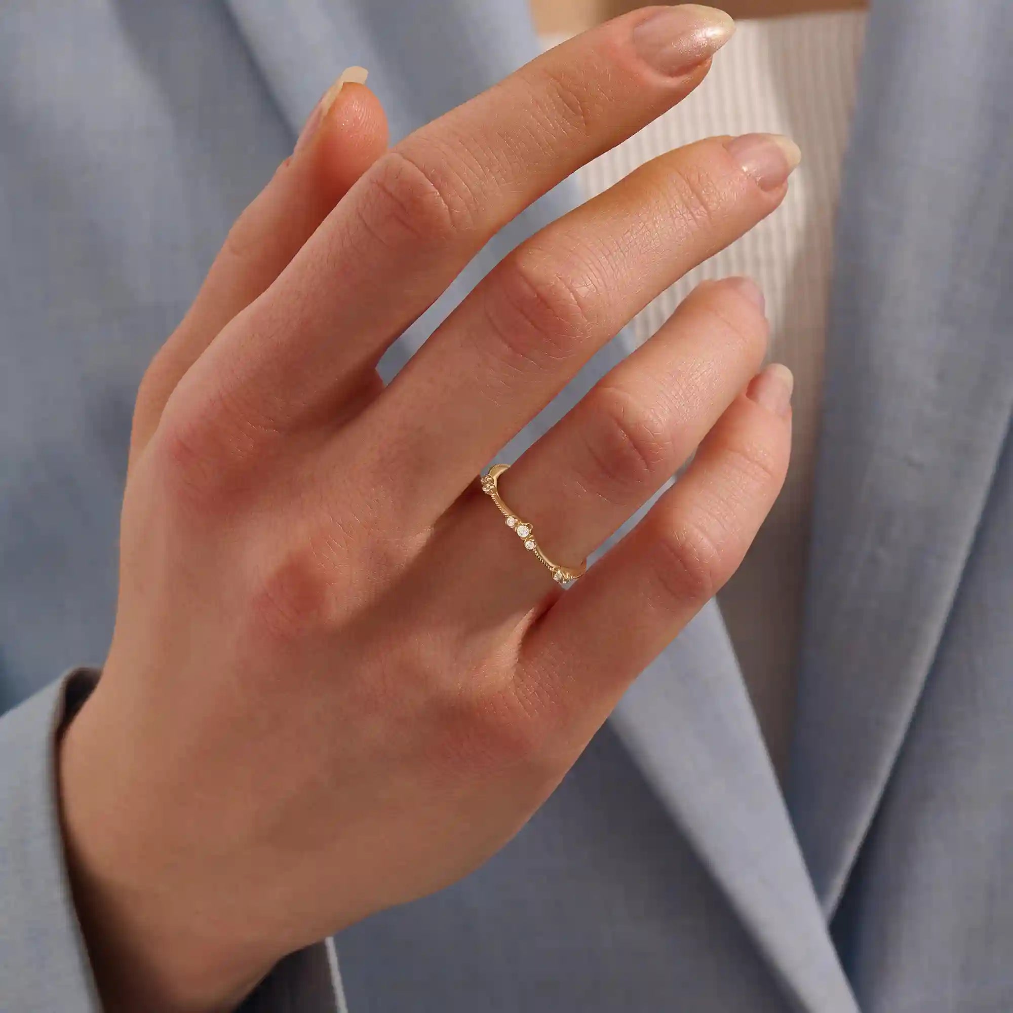 Model wears a slim vintage-style curved ring with moissanites on a delicate milgrain band. A refined stacking piece with intricate craftsmanship.