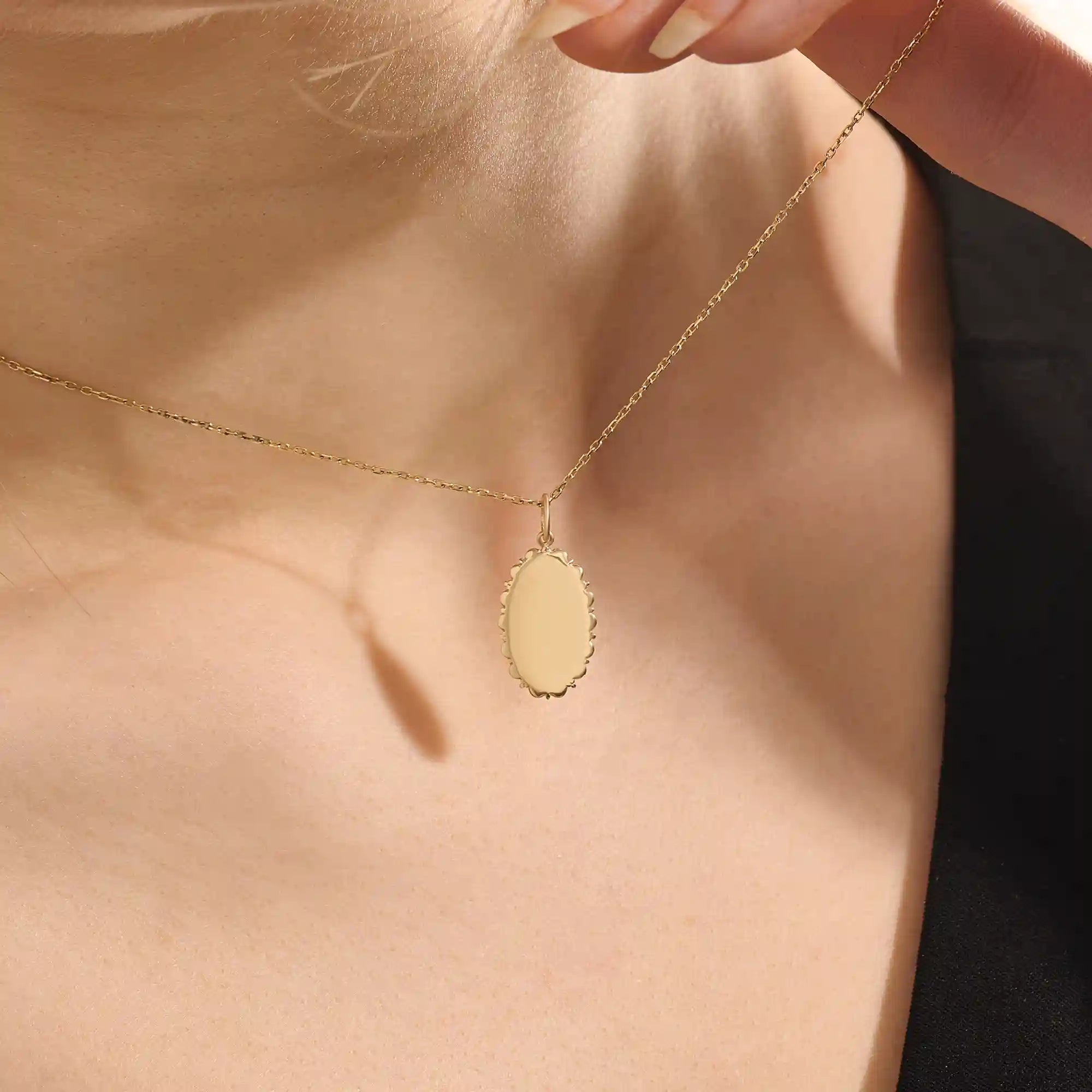 Model wears an oval plain pendant necklace in 14k gold, ideal for personal engravings. A sleek and versatile everyday accessory.