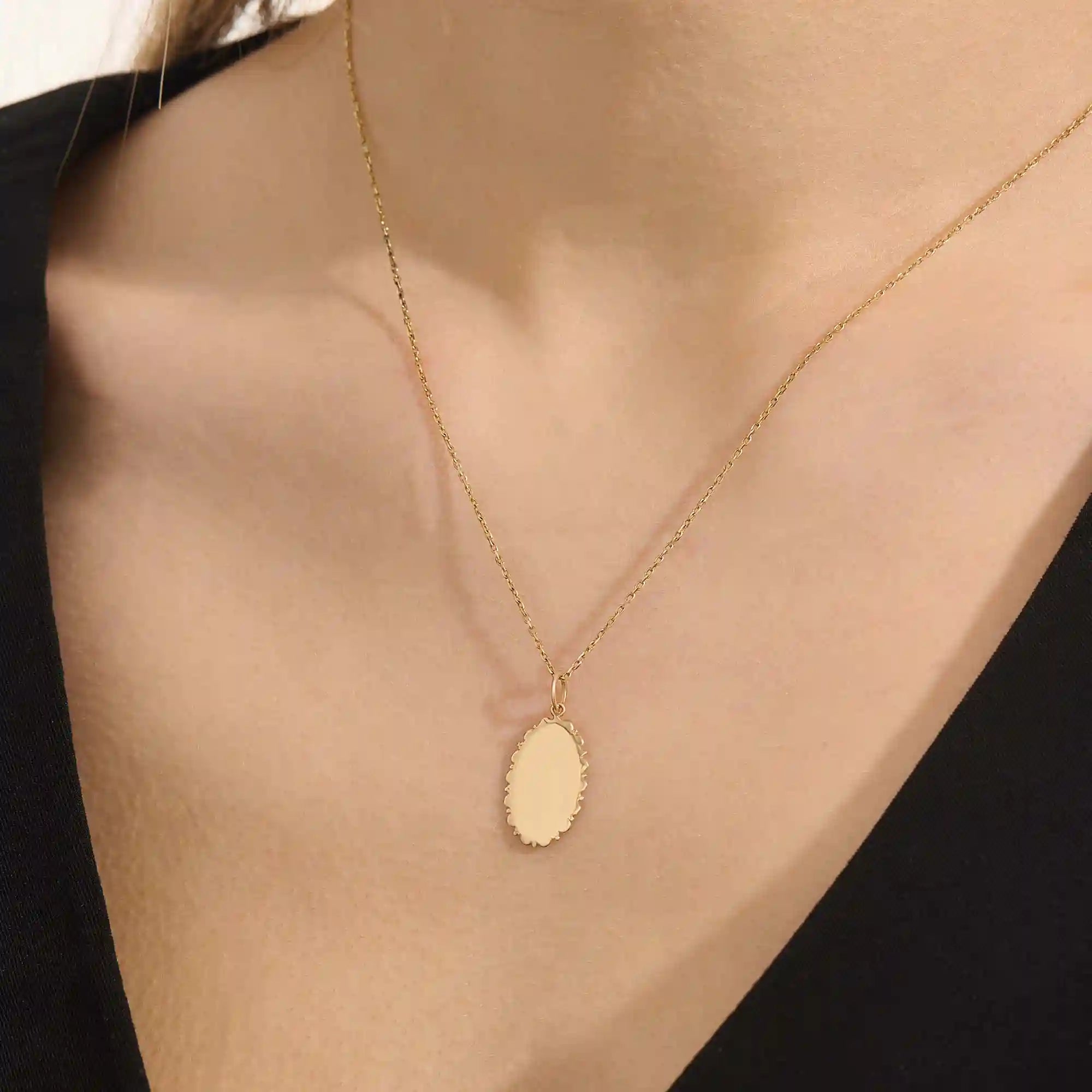 Model wears an oval plain pendant necklace in 14k gold, ideal for personal engravings. A sleek and versatile everyday accessory.