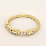 Side angle view of a 14k solid yellow gold band with baguette cut moissanite center stone and round brilliant cut moissanite accents in a modern bezel and prong setting